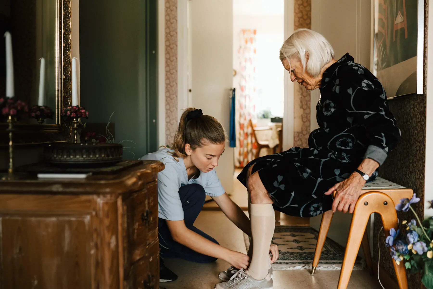 Carer helping pensioner put on shoe in her house