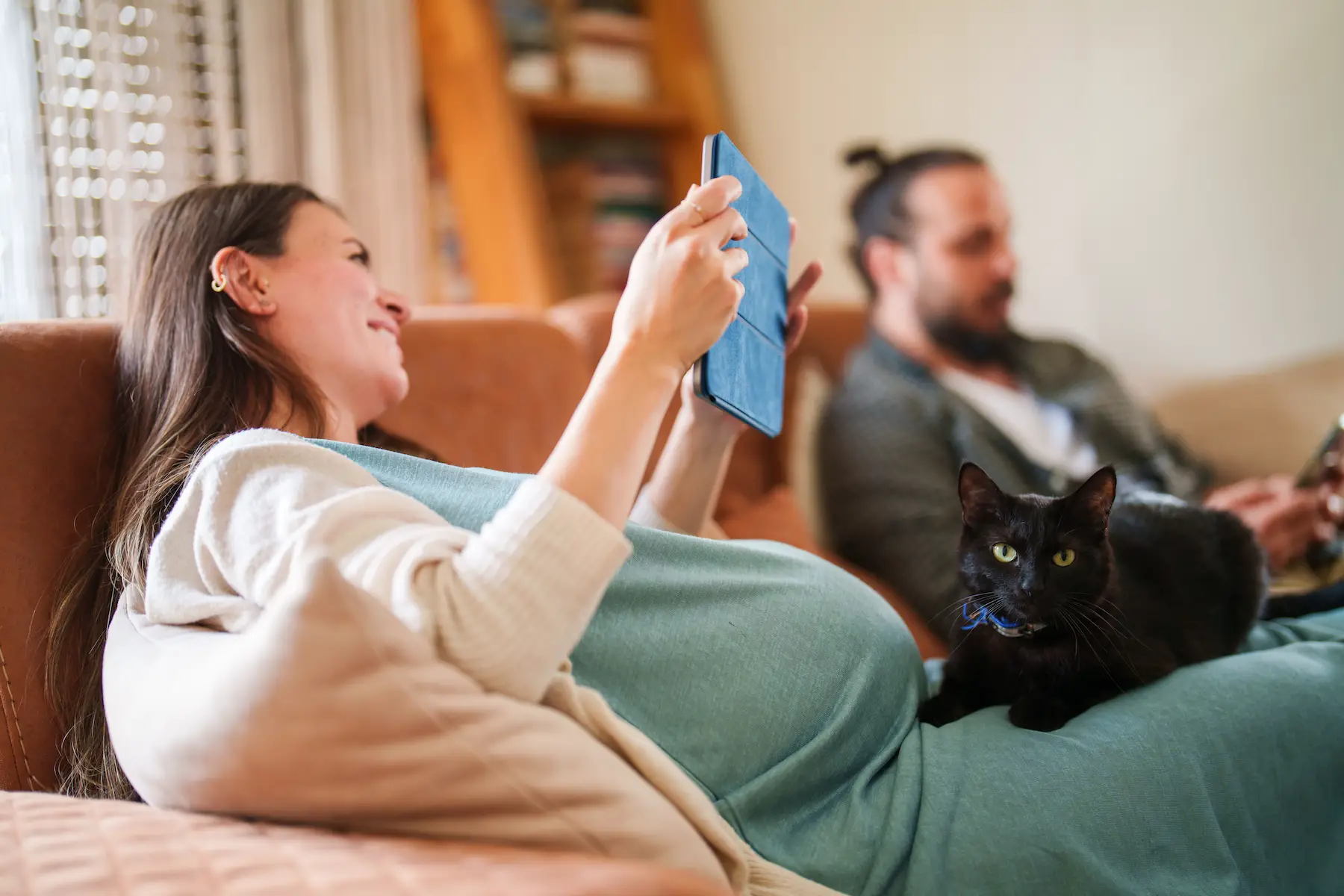 A black cat sits proudly on the lap of its pregnant owner staring directly at the camera
