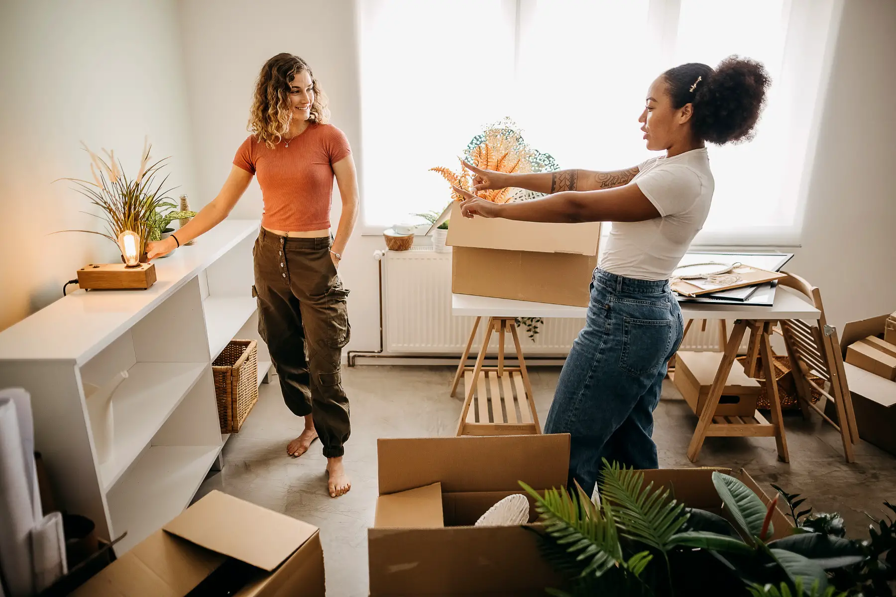 two female students unpacking boxes in an apartment and deciding where to place items