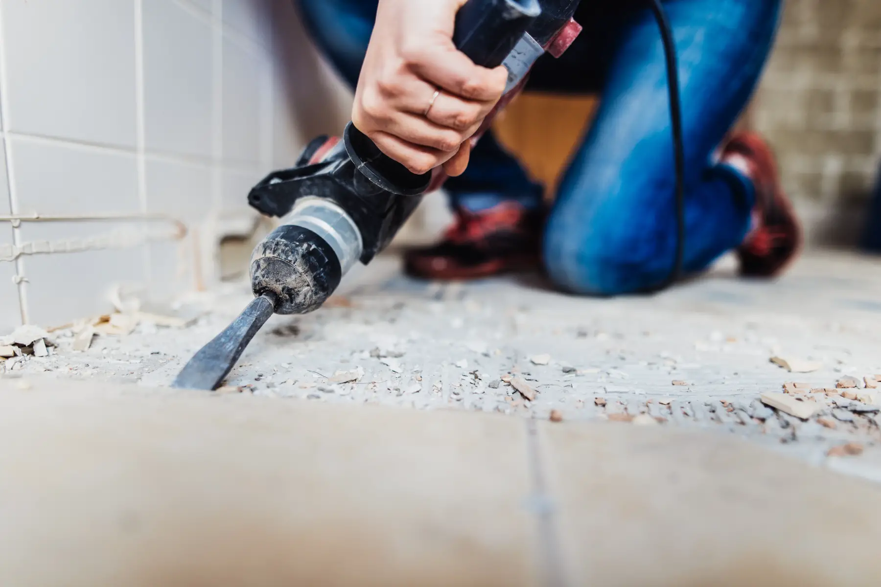 a close-up shot of someone removing old tiles from a floor using a heavy piece of equipment 