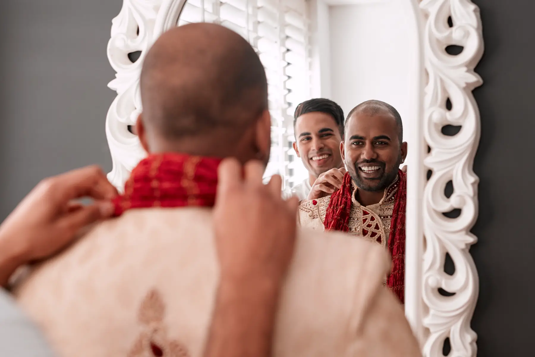 Muslim groom looking into mirror while friend helps him to get ready