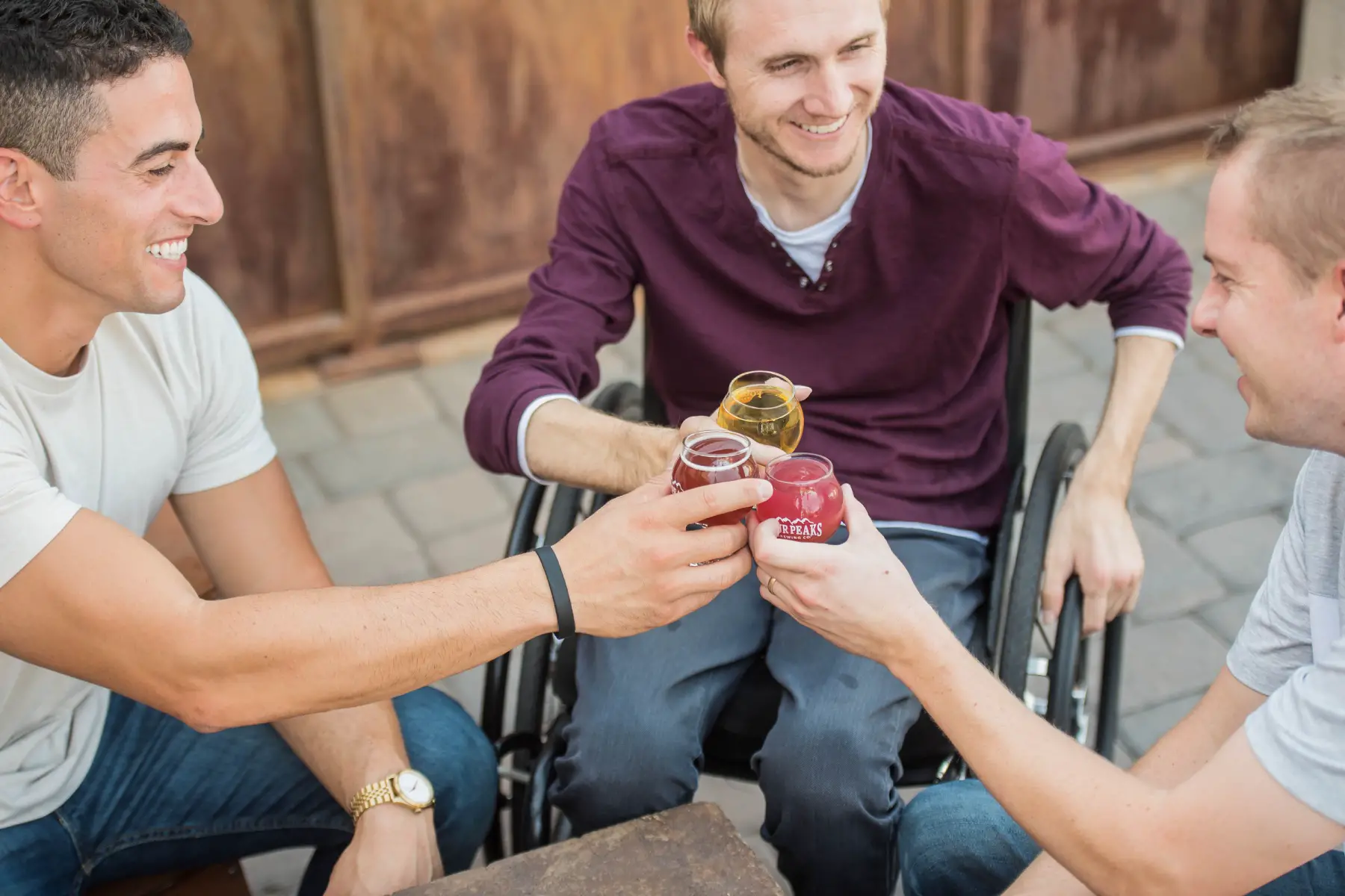 a group of three friends sitting in a circle and socializing over a drink, one sits in a wheelchair