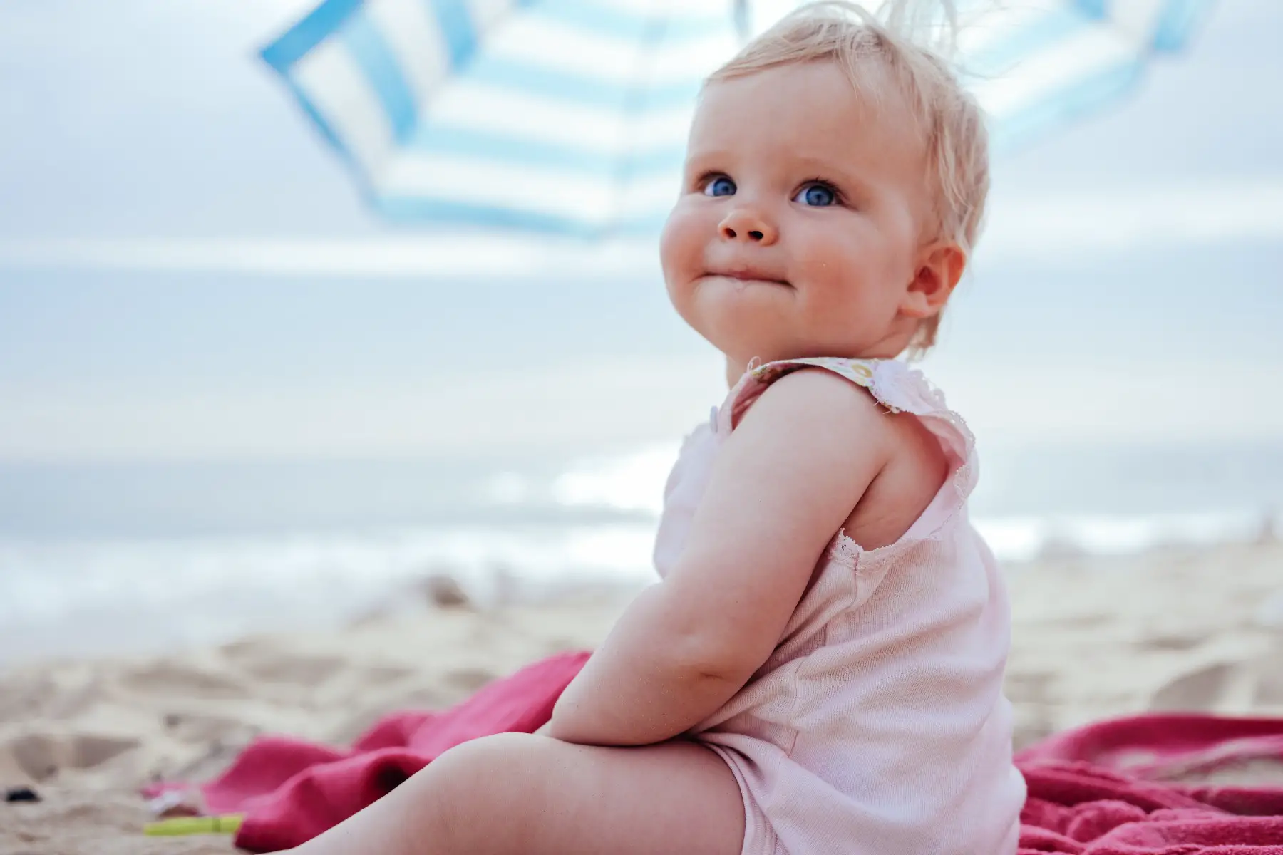 Happy little fat baby with giant blue eyes sitting at the beach, drooling.