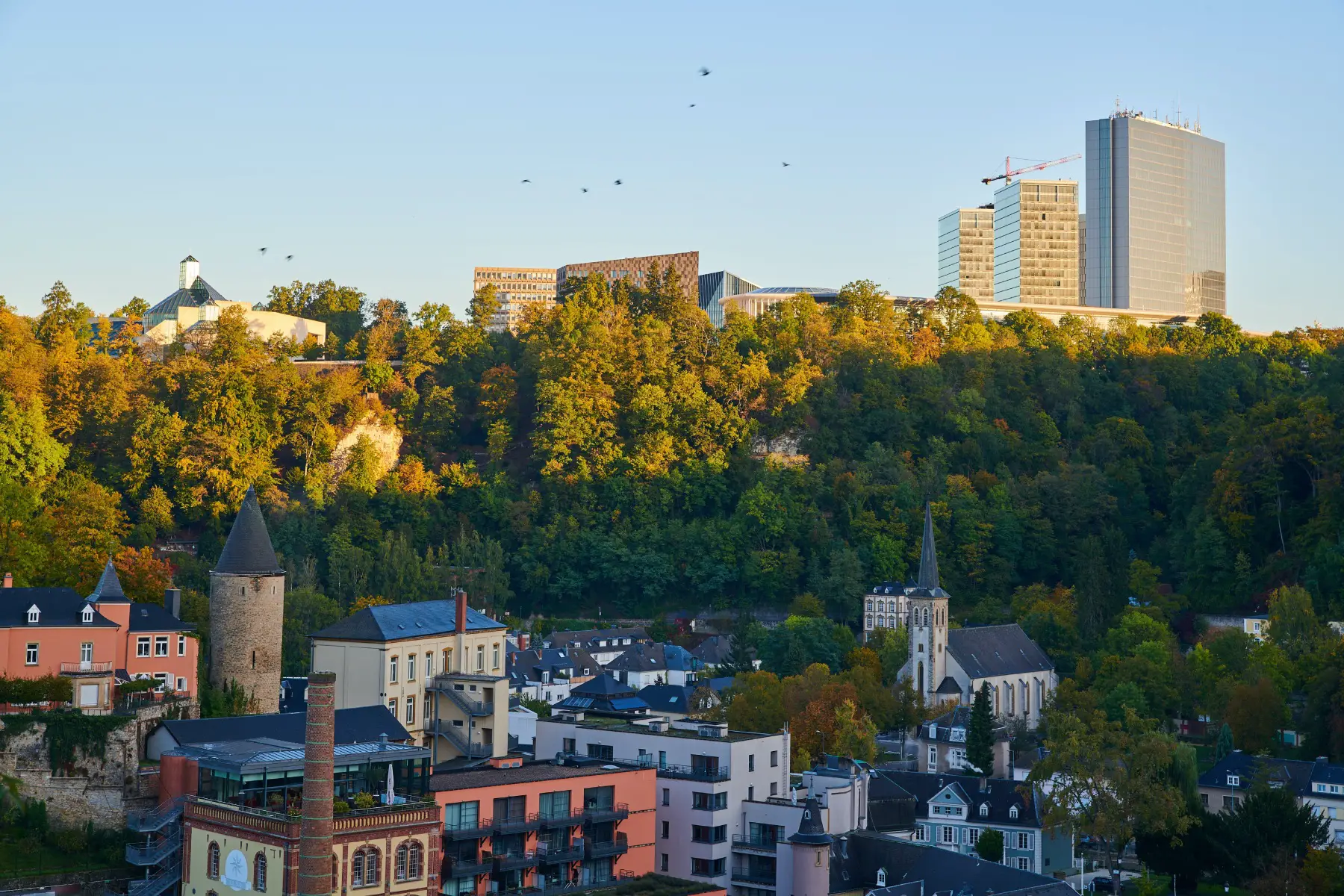 A landscape view of the sun setting over Luxembourg City, with tall buildings in the background