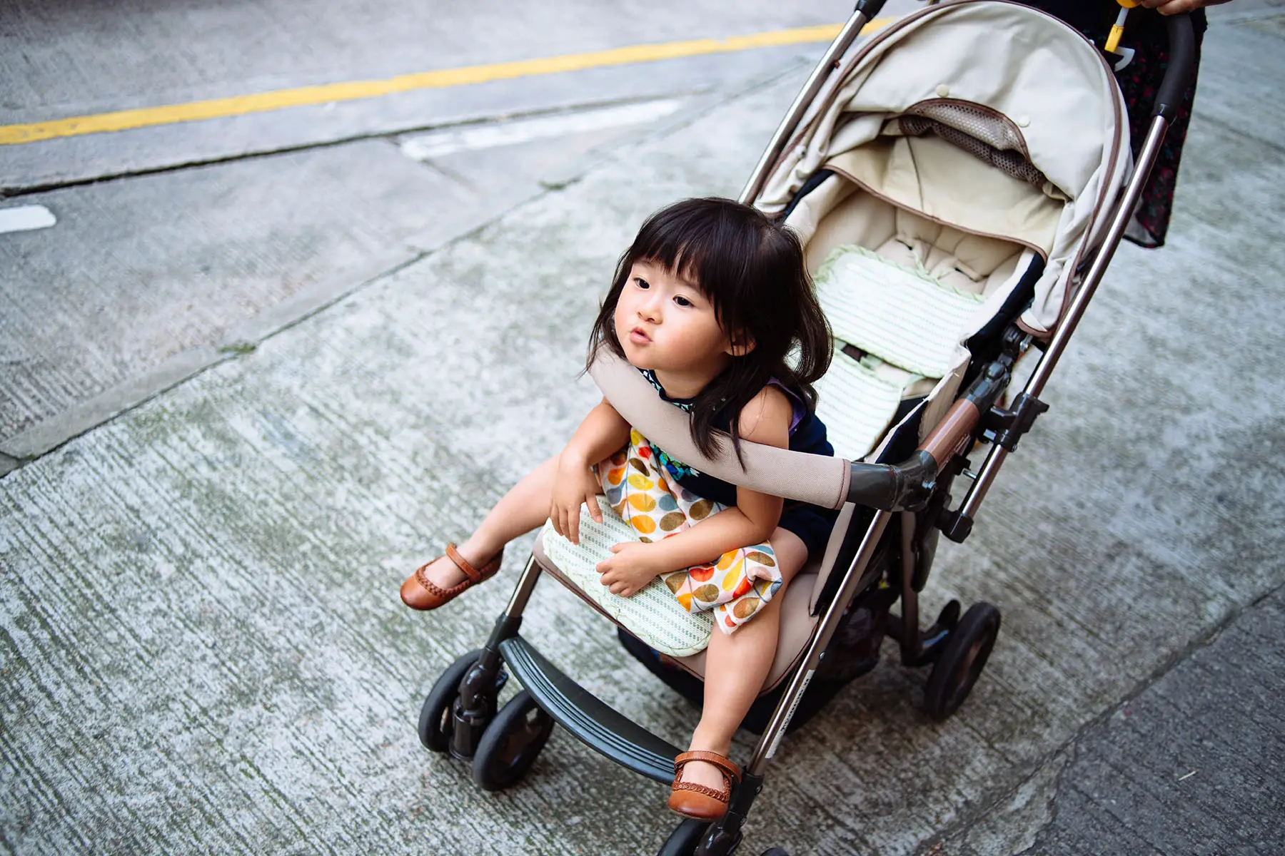 Toddler girl sitting on stroller and leaning her chest on the front handle, sighing.
