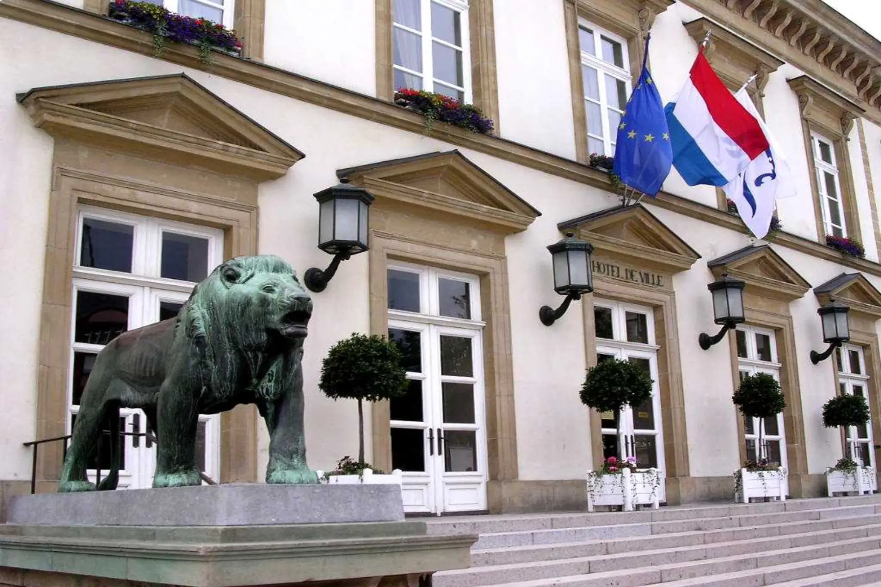 Exterior of Hôtel de Ville (Town Hall), Luxembourg, huge lion statue in front and flags above door.