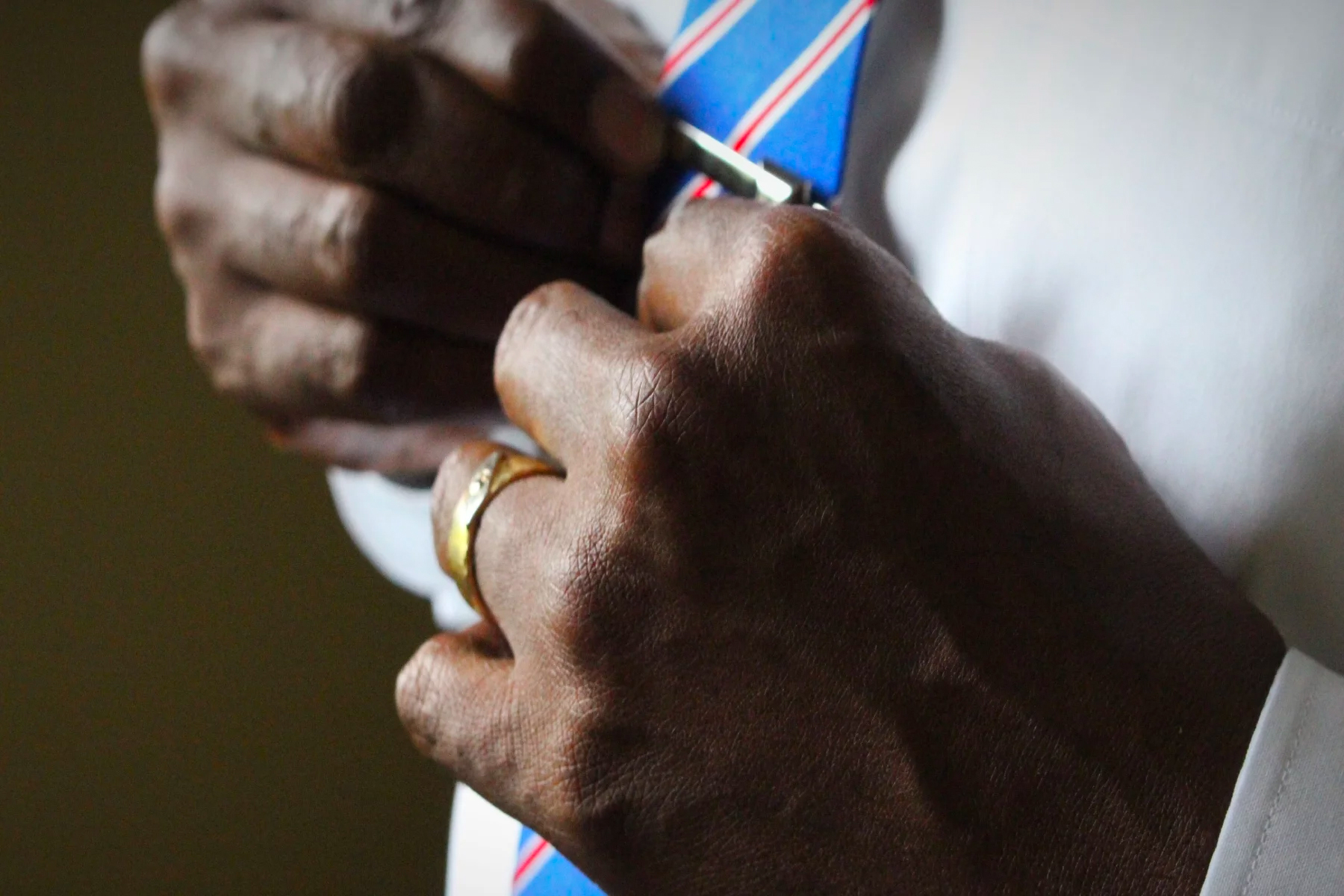 Close up of man's hands with wedding band adjusting a tie pin