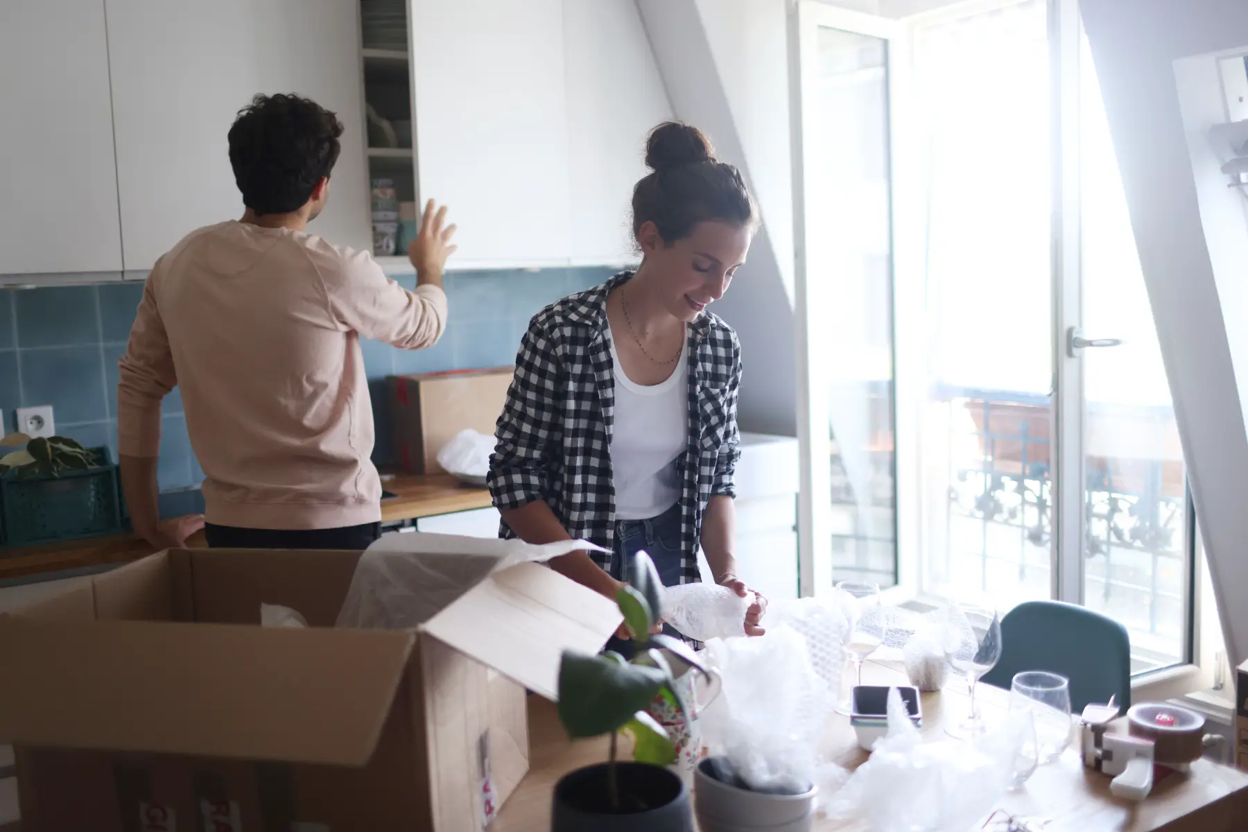 a couple packing up items in the kitchen using bubblewrap and cardboard boxes