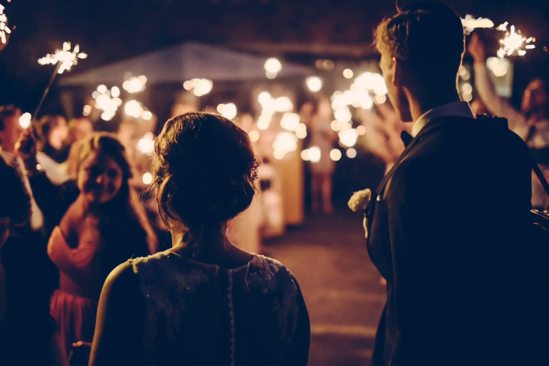Nighttime wedding - silhouette of bride and groom being welcomed by guests at reception with sparklers