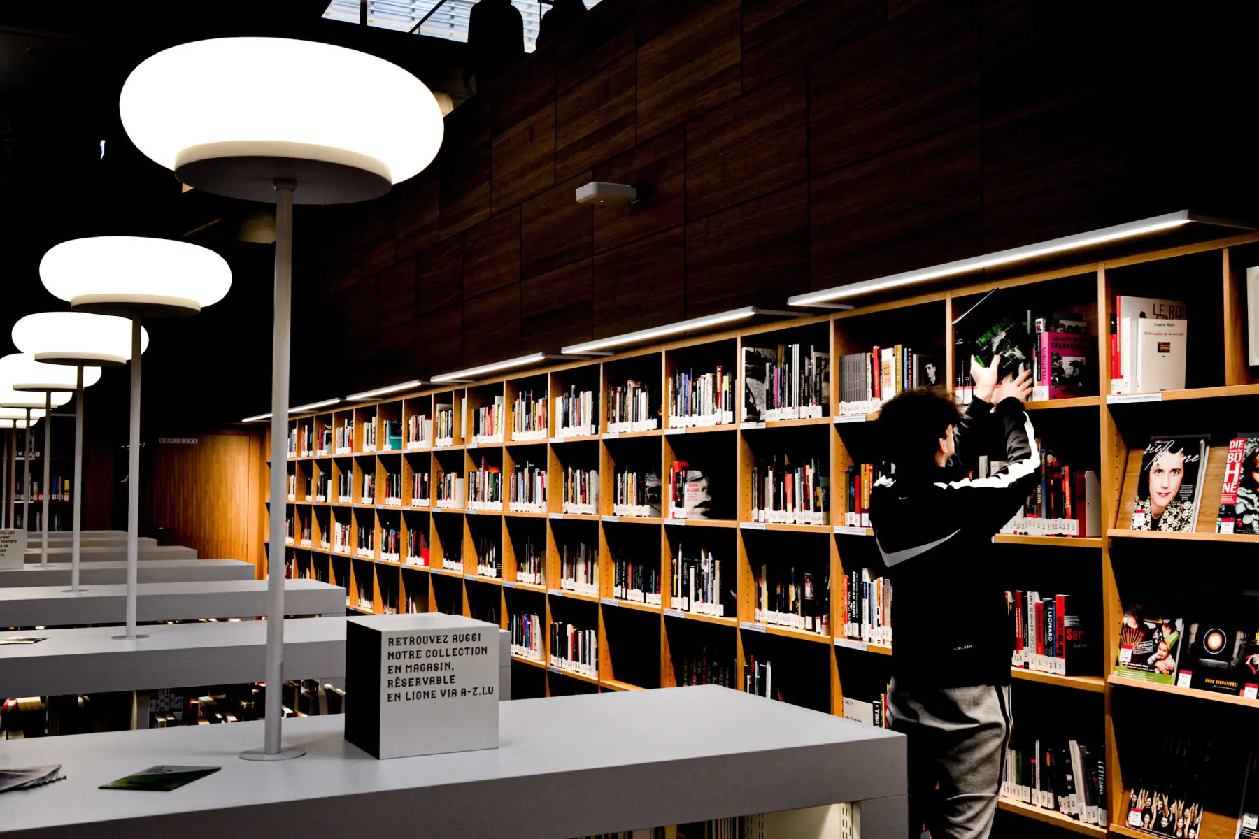a male student reaching up to take a book off the shelf at a library in Luxembourg