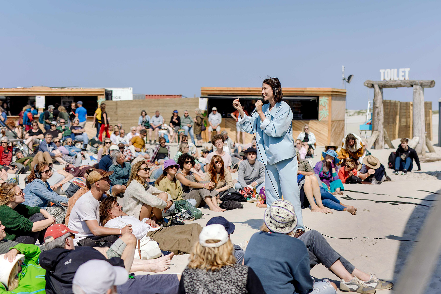 Large crowd sitting on the ground to listen to a performance by Marleen Annema, during Oerol Festival 2023.