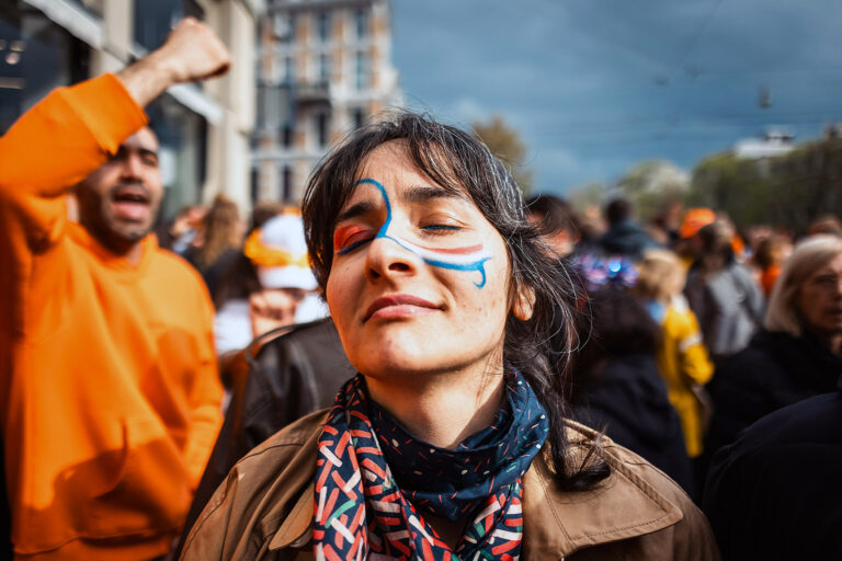 Woman with red, white, and blue face paint, has her eyes closed as she enjoys a sunny moment during kings day.