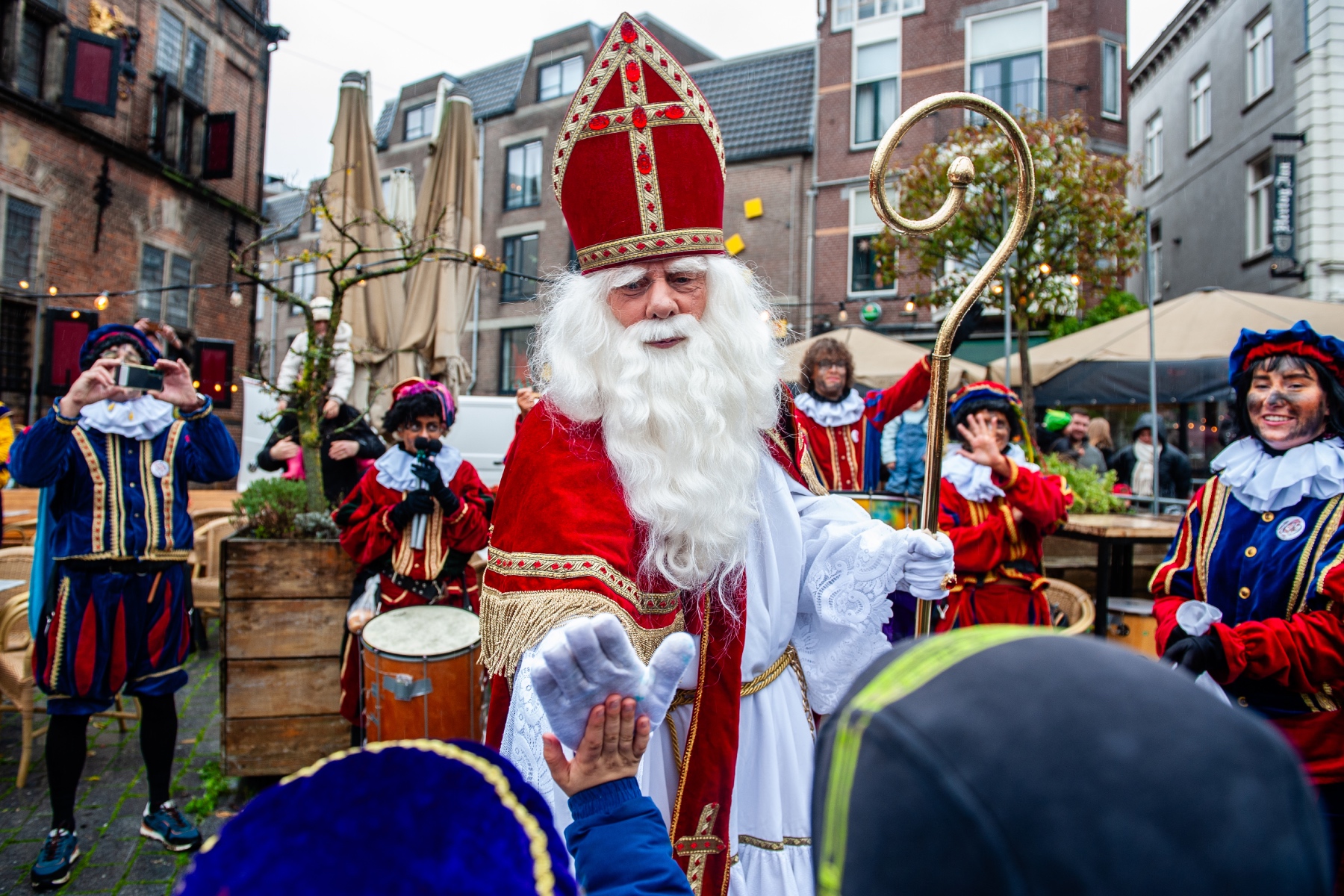 Sinterklaas gives children high-fives while two Piets stand behind him