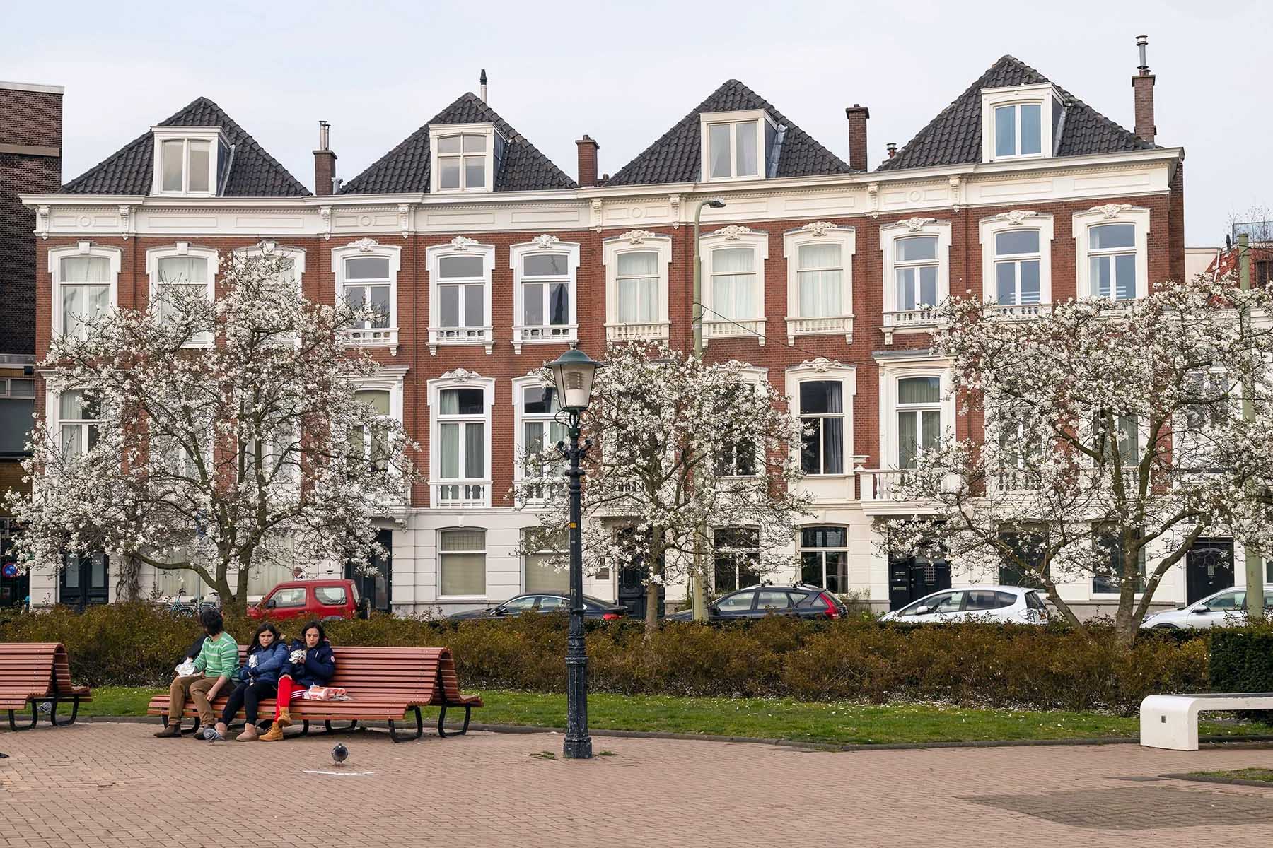 Three people sitting on a bench, with large houses in the background. They're at Prins Hendrikplein, an expensive neighborhood in The Hague.