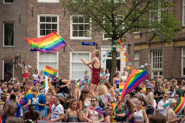 Large crowd of people gathered to celebrate Amsterdam Pride. There are loads of rainbow flags.