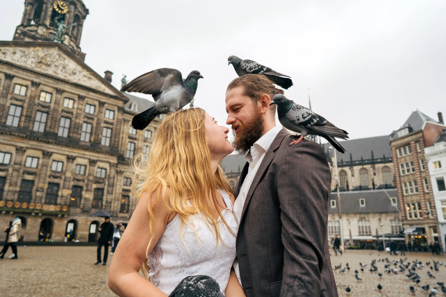 a smiling bride and groom looking at each other as they stand in front of the Royal Palace Amsterdam surrounded by pigeons 