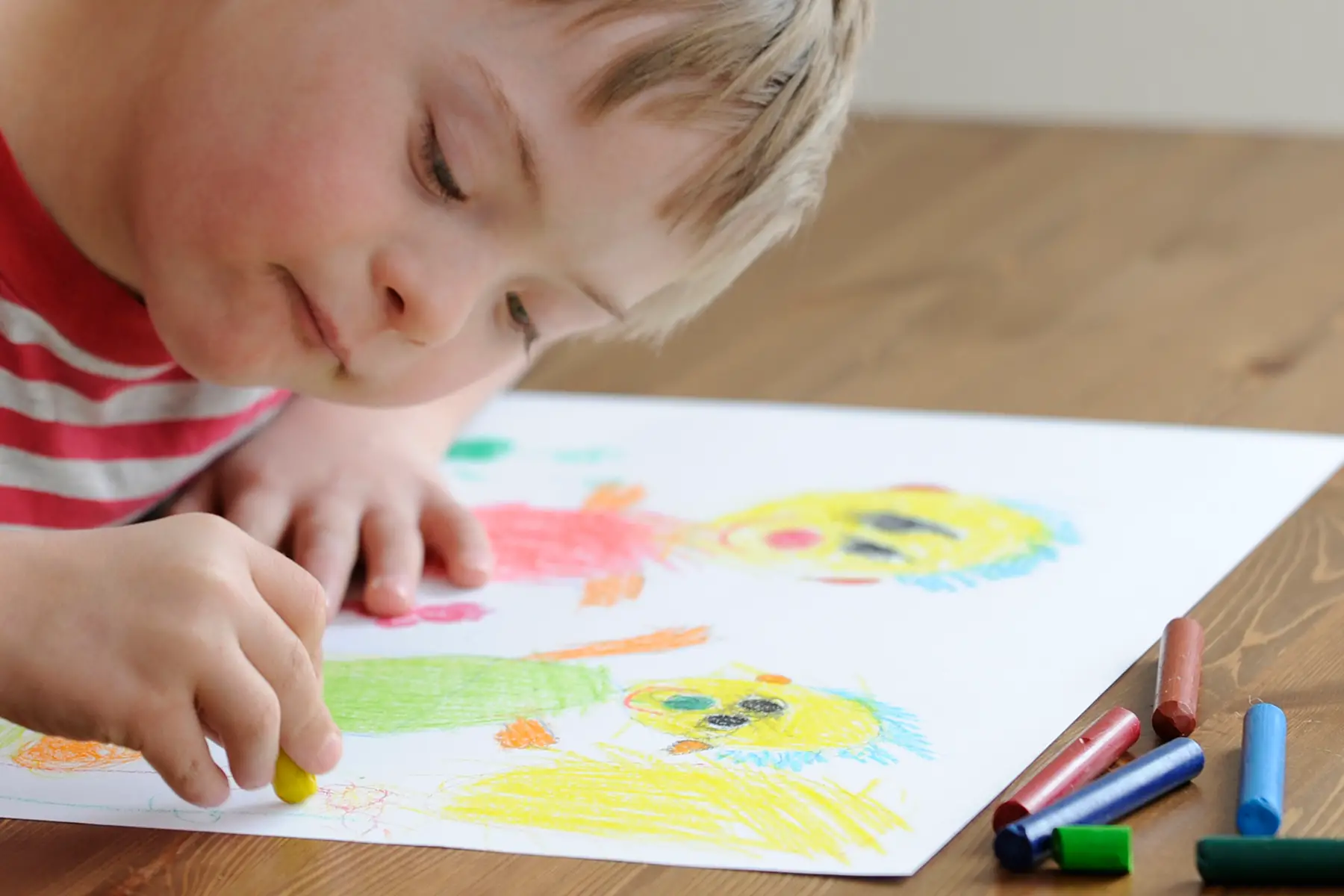 A child with Down's Syndrome drawing a picture in crayon of two people.