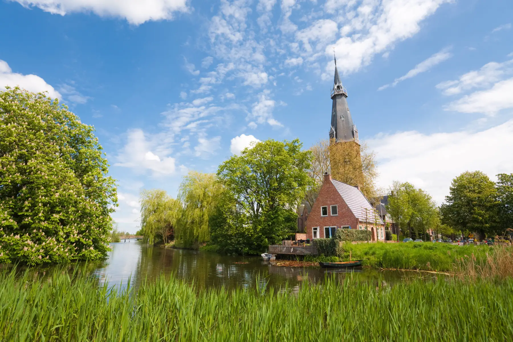 A scenic rural view of a church in Amstelveen surrounded by green fields and water