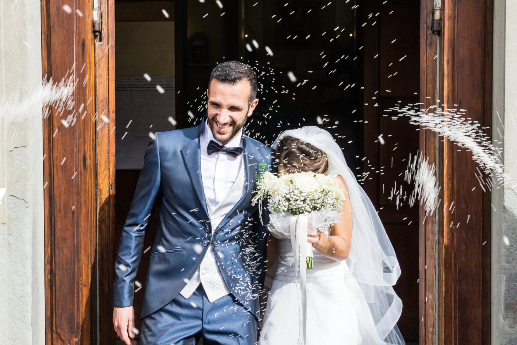 confetti being thrown on a happy newlywed couple as they exit a church