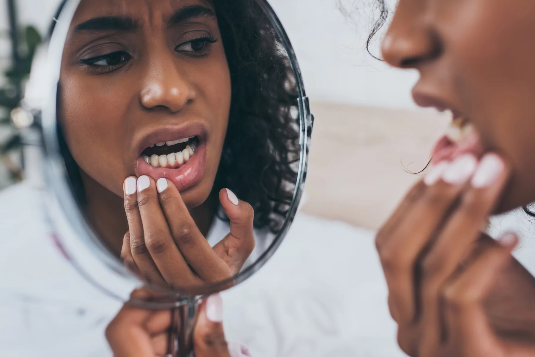 a woman looking into a mirror while suffering from tooth pain