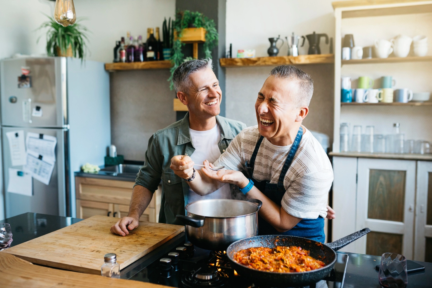 a male same-sex couple chatting and laughing together in a kitchen