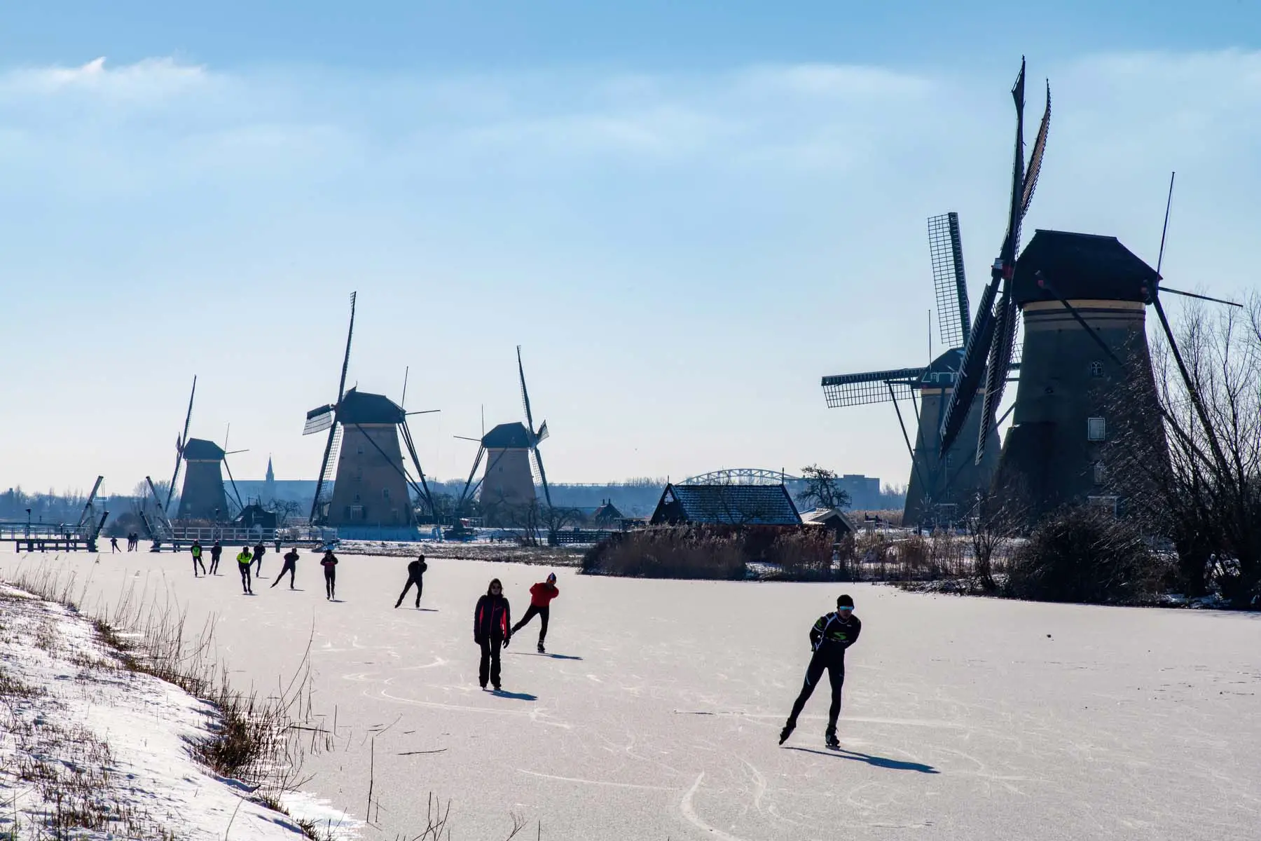 ice skaters on frozen lake near line of Dutch windmills