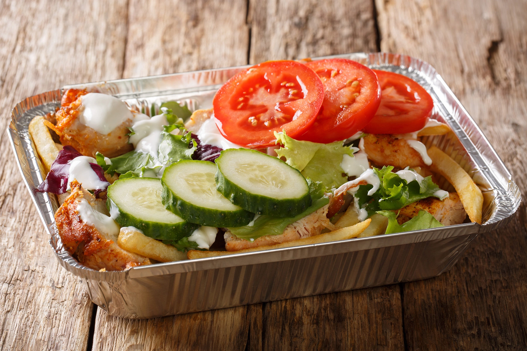 Kapsalon: chips with meat and salad on top in an aluminium takeaway tray