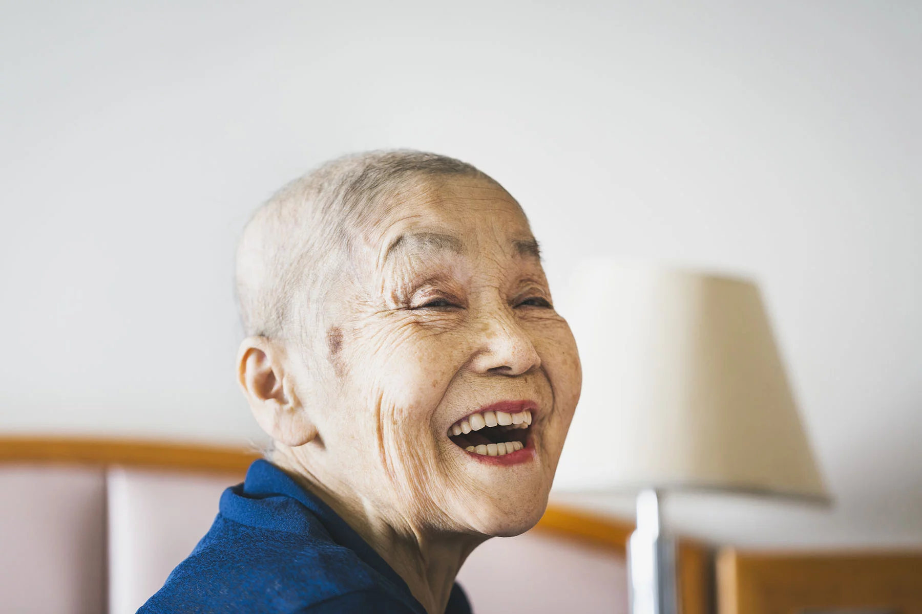 A senior woman whose hair has fallen out due to her cancer treatment is smiling a beautiful smile.