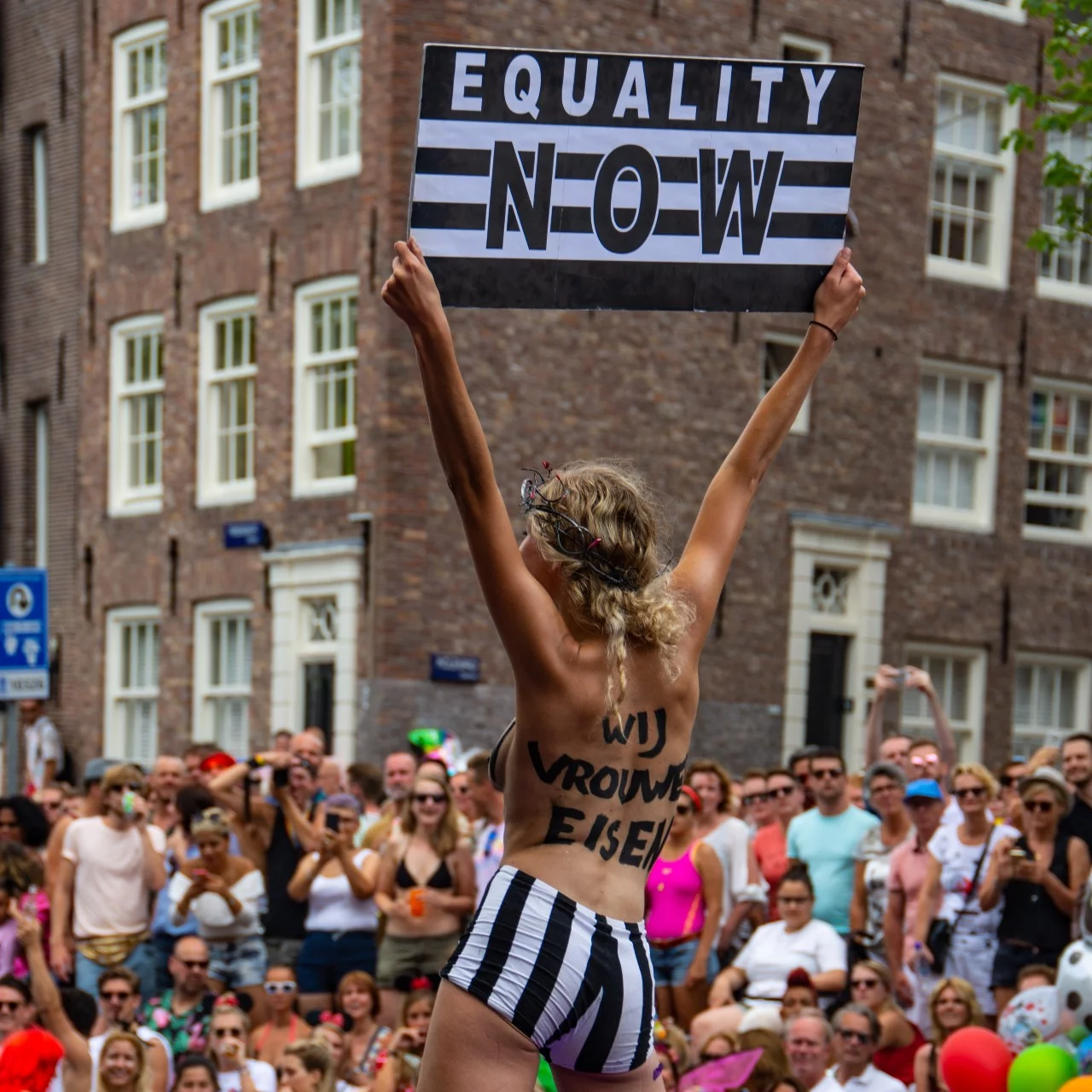 Woman holding an Equality Now sign. On her back, she has written: 