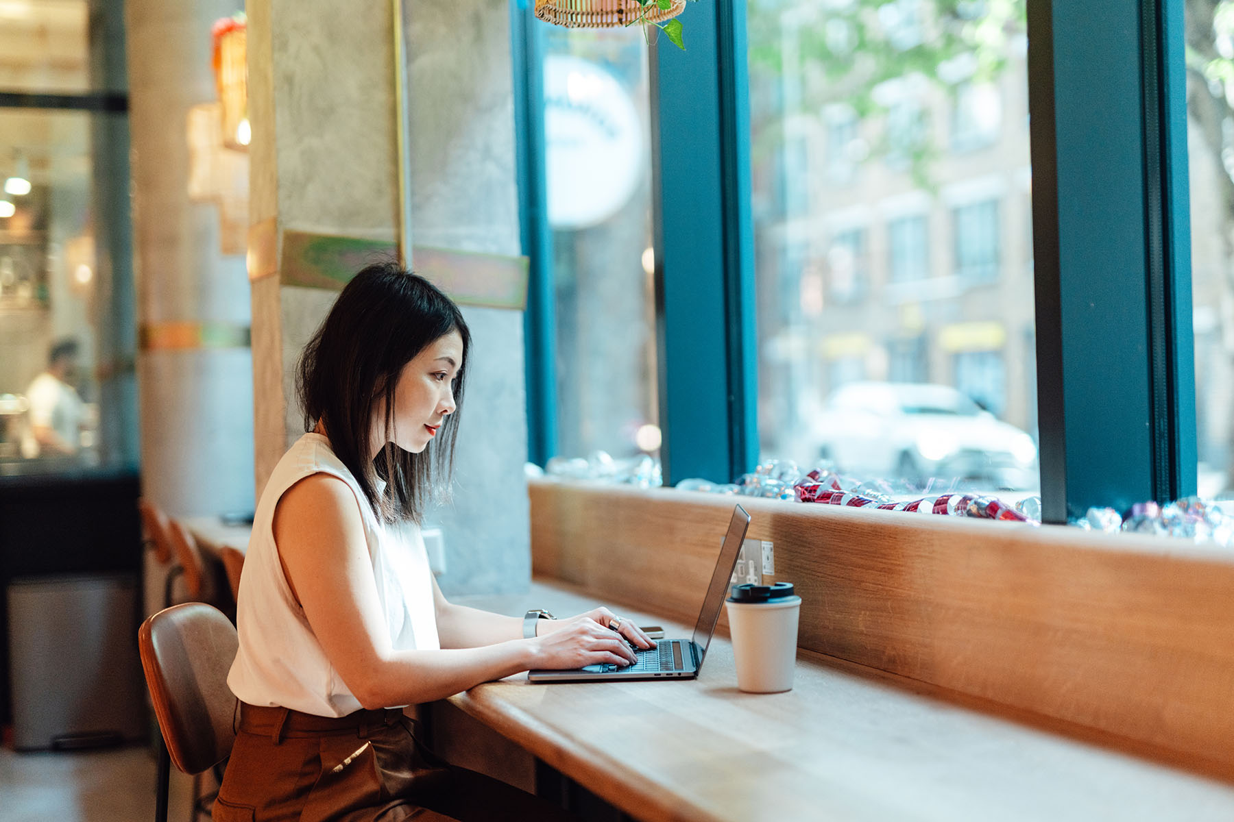 Woman working with laptop while drinking coffee at cafe.