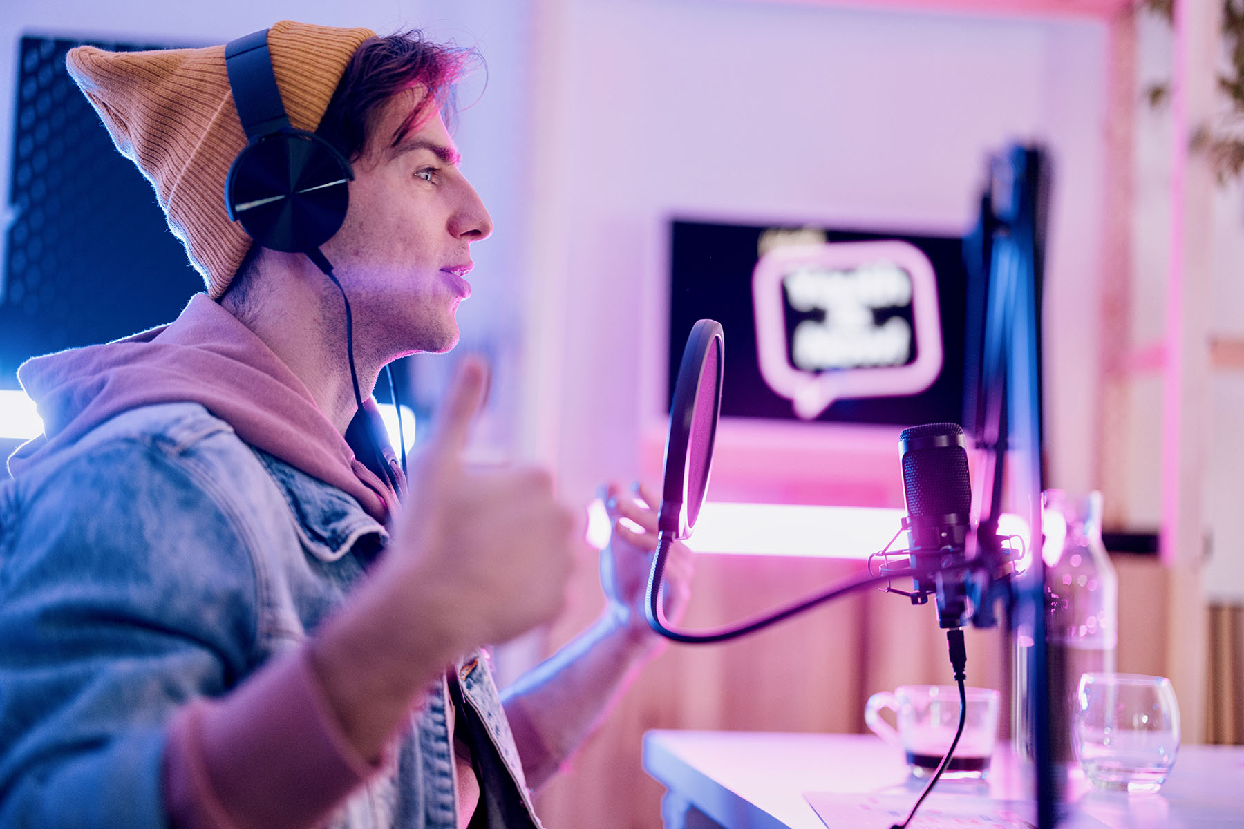 Man wearing a beanie and headphones talking into a professional-looking microphone.