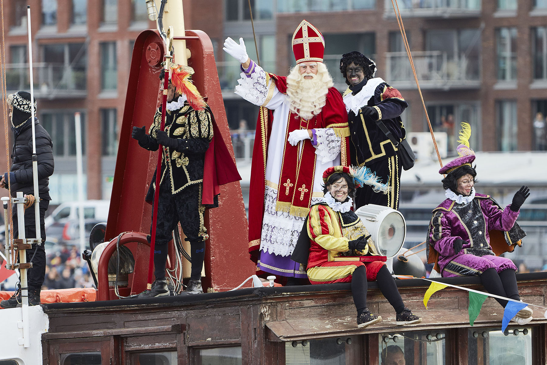 Sinterklaas and a couple of Sooty Petes are standing on top of the steam boat waving to the people down on the quay.