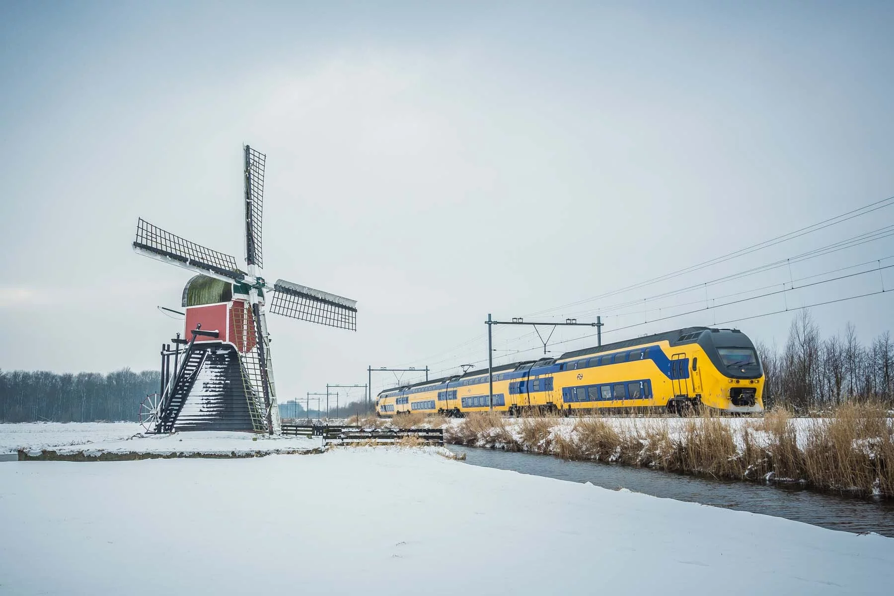 An NS Intercity train passing a windmill on a snowy day