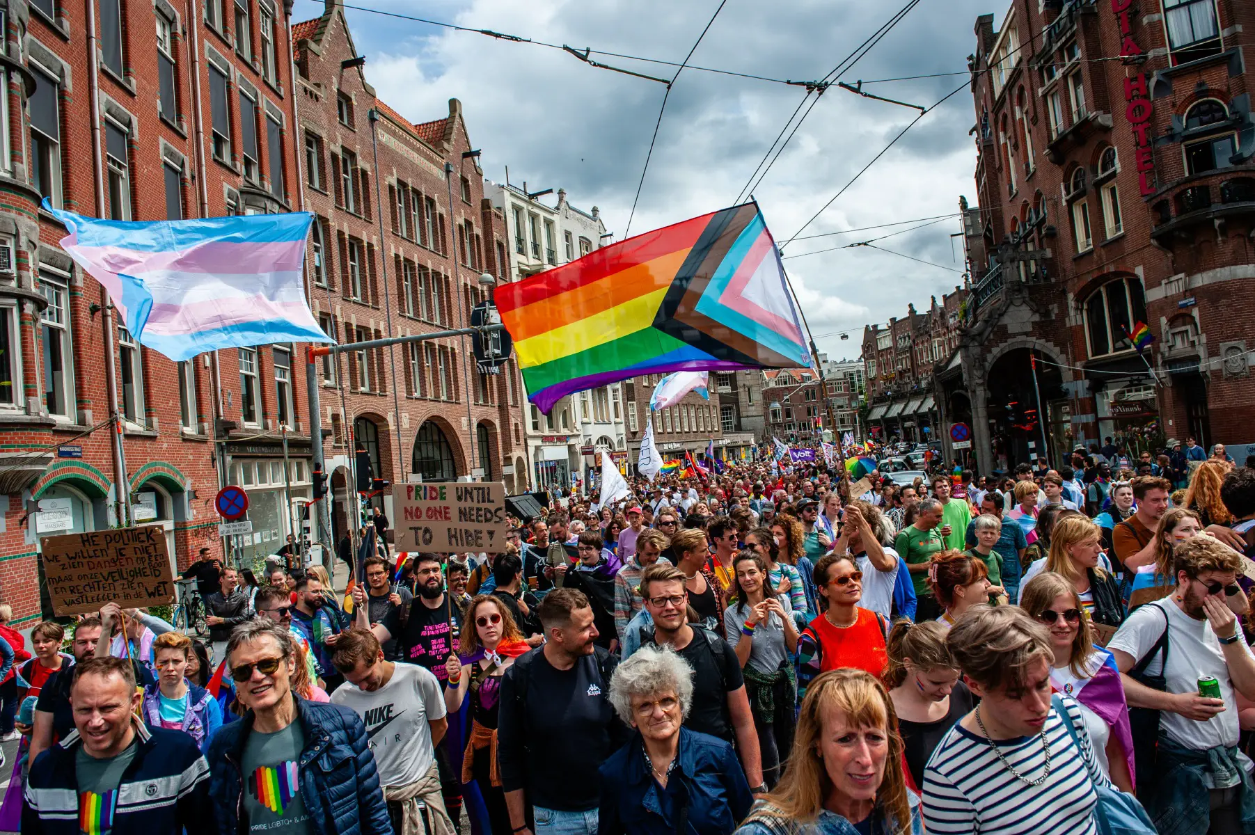 People participate in Pride Walk in Amsterdam waving pride and transgender flags