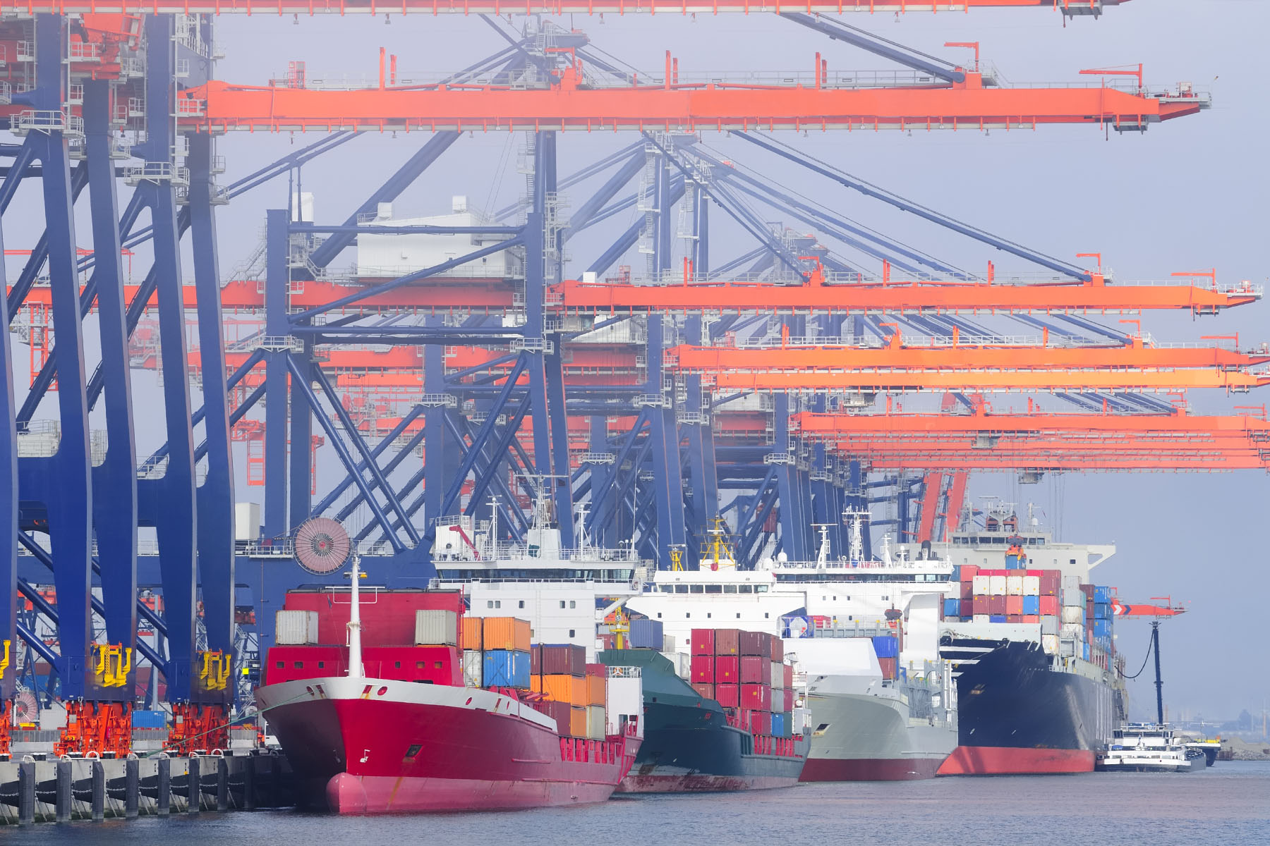 Container terminal in the port of Rotterdam in The Netherlands with four container ships being loaded and unloaded by massive cranes.