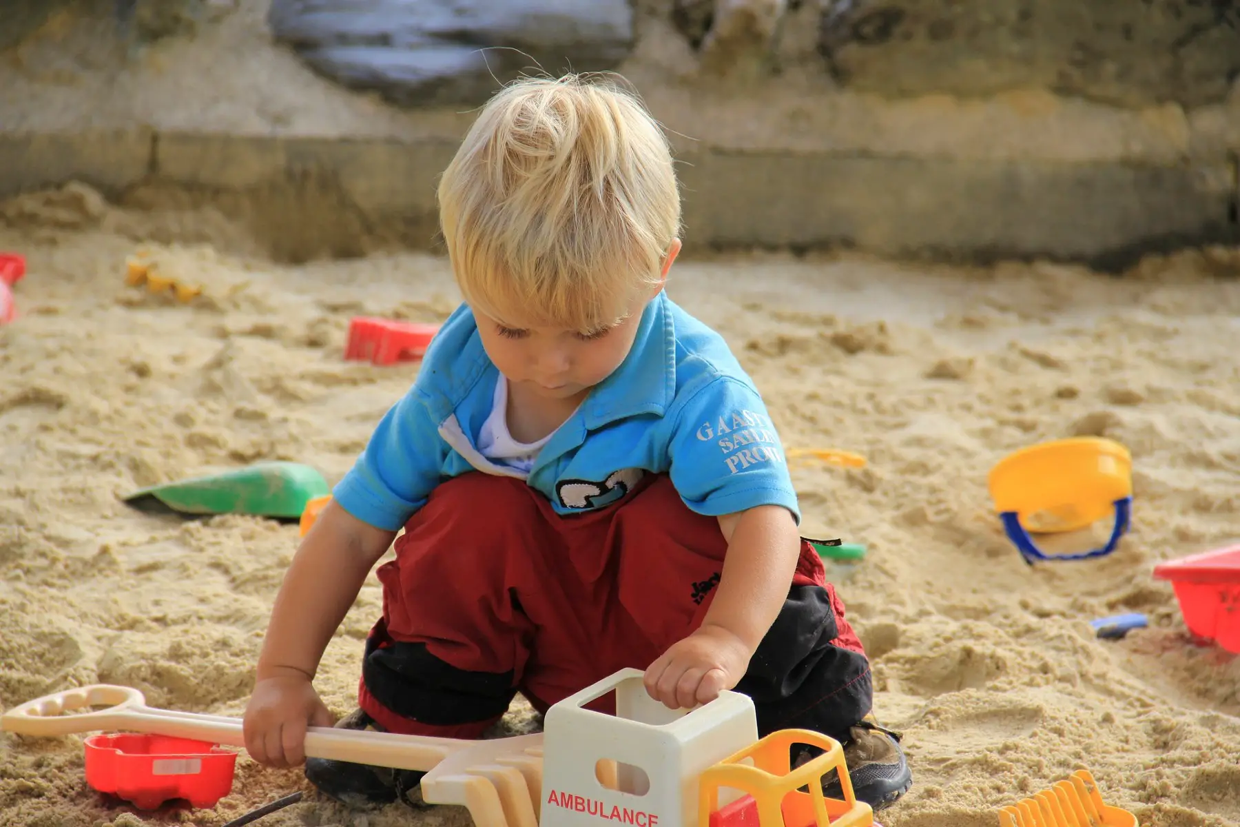 Little boy playing in the sandbox with a toy ambulance