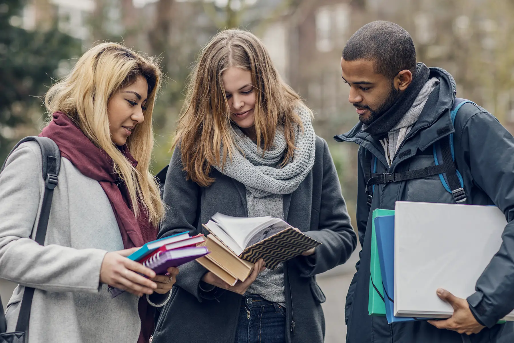 Three students standing in a row, looking at books together