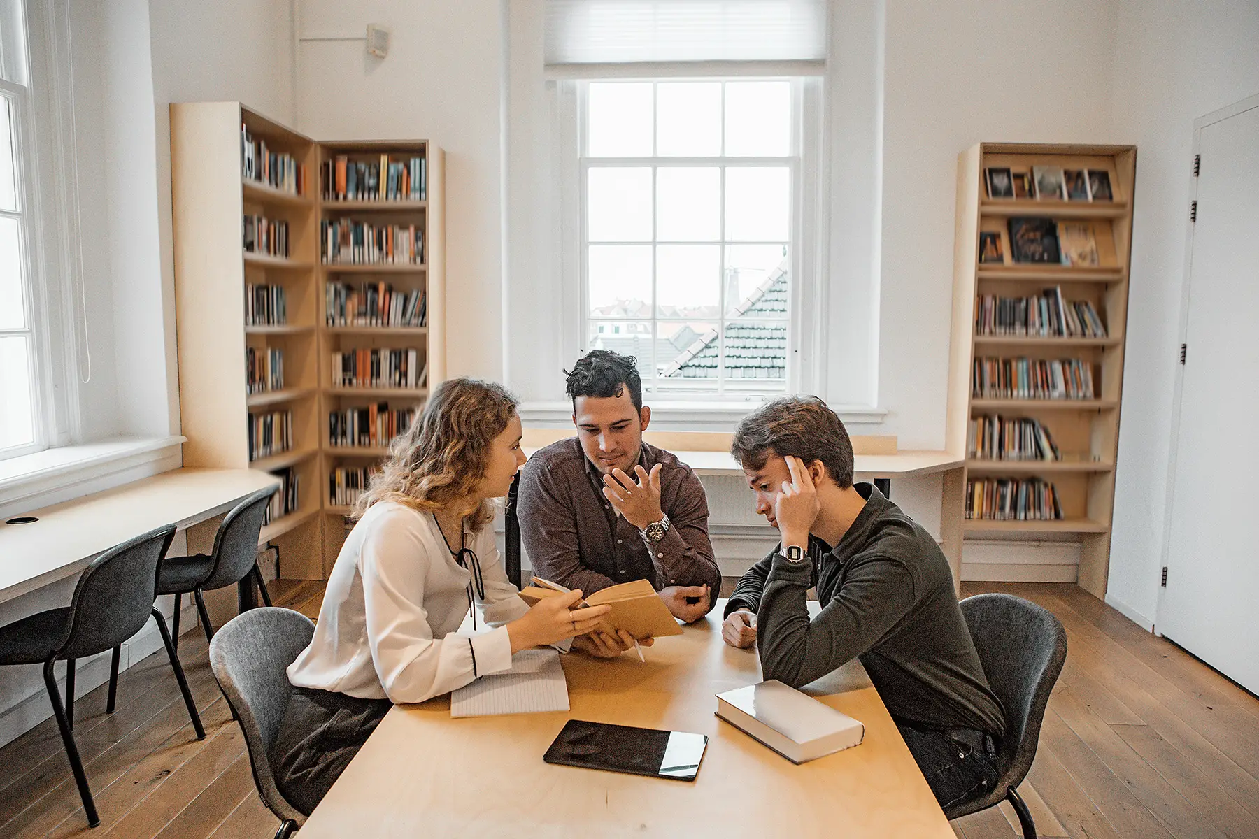 Three students sat at a table, studying together in a library
