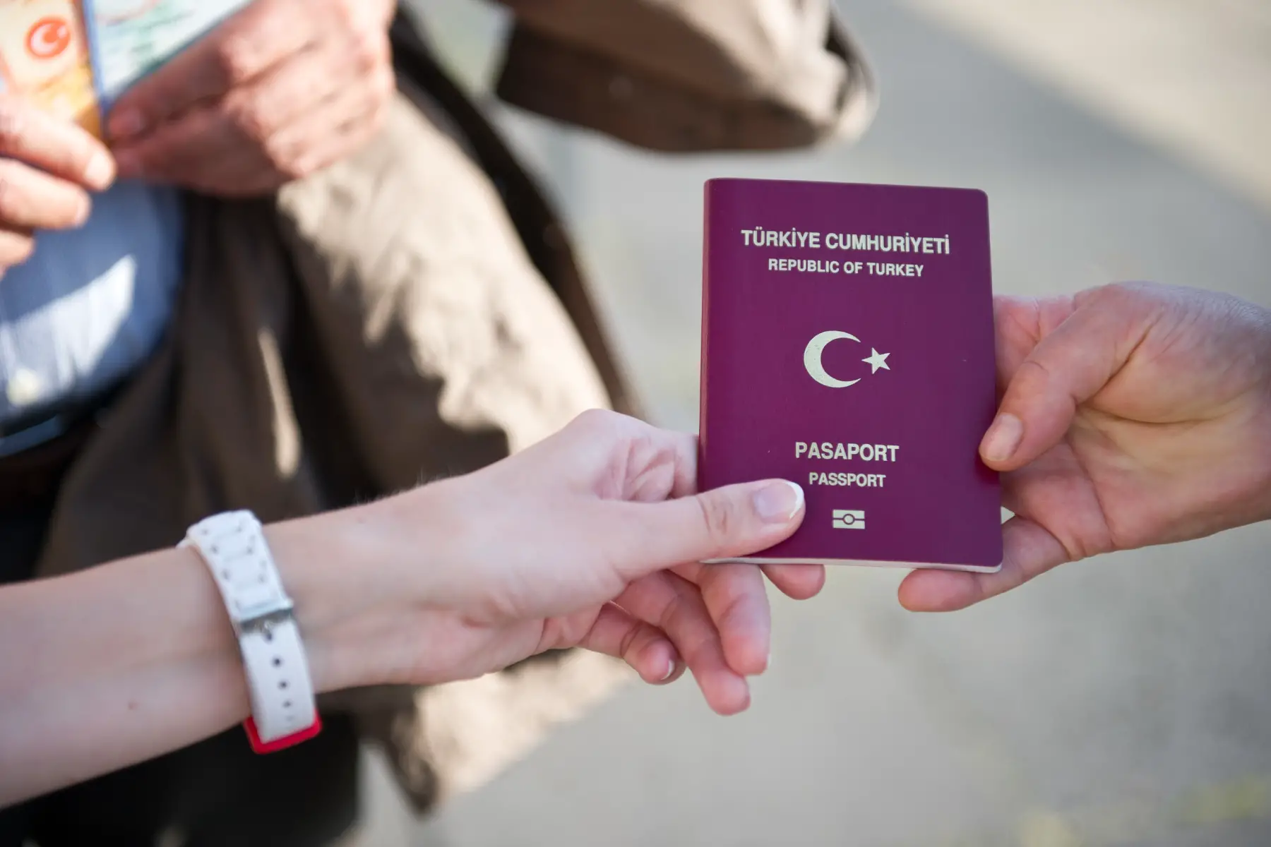 Two people pass a Turkish passport between them