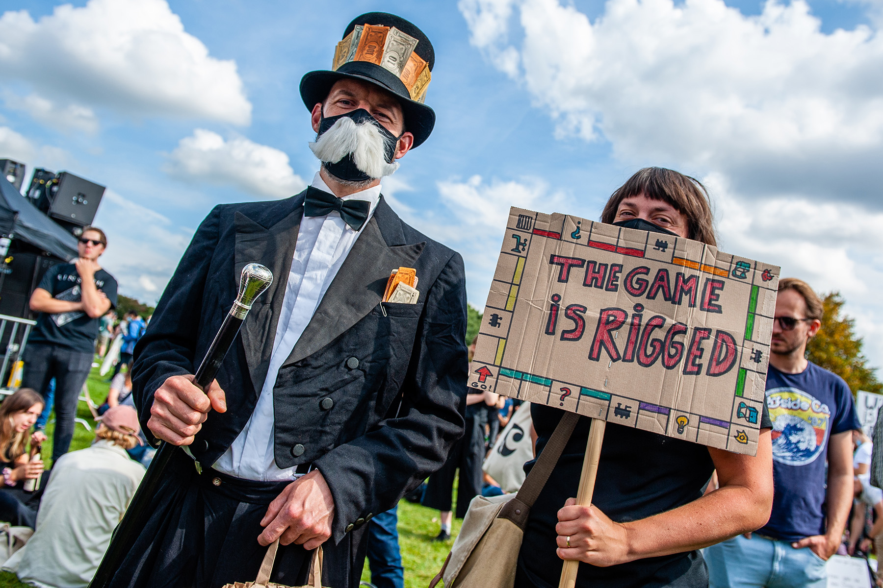 Protester is dressed as the monopoly man, while another is carrying a monopoly sign that says "the game is rigged".