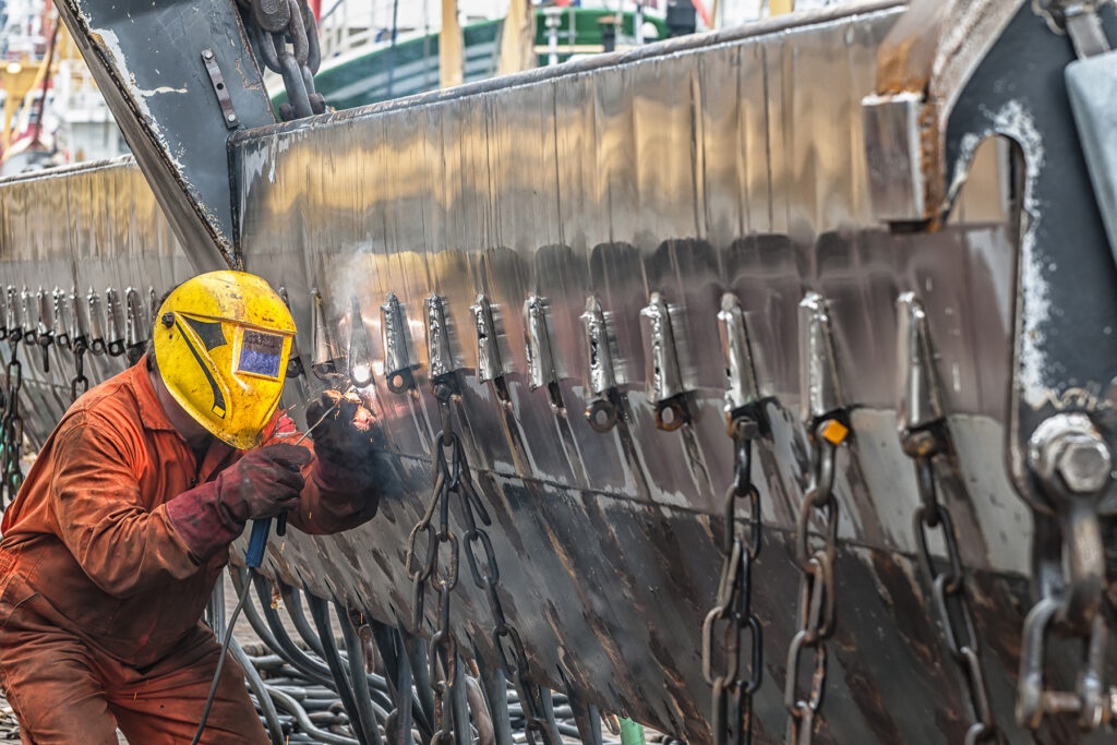 A worker is using a laser to weld the wall of a ship.