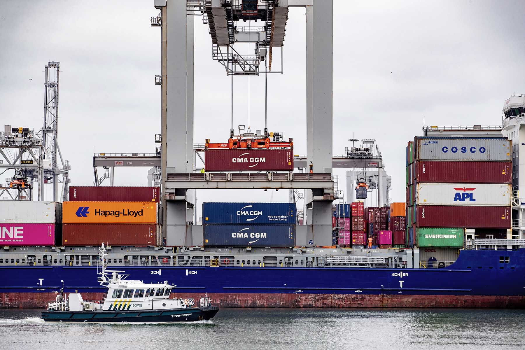 A Customs boat is sailing past a cargo ship filled with containers in Rotterdam Harbor, the Netherlands. 