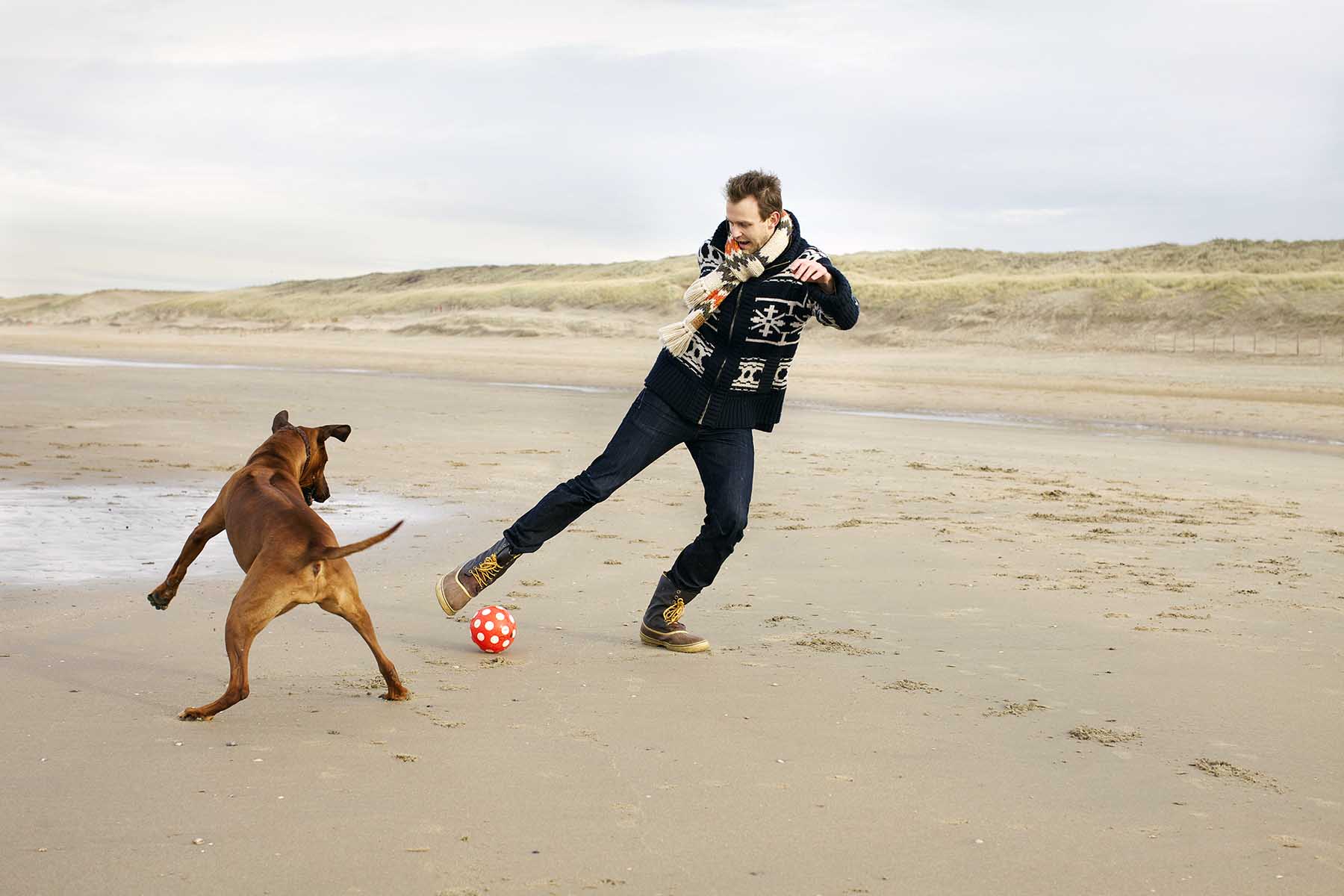 Man playing football with his dog at the beach of Bloemendaal aan Zee, the Netherlands.