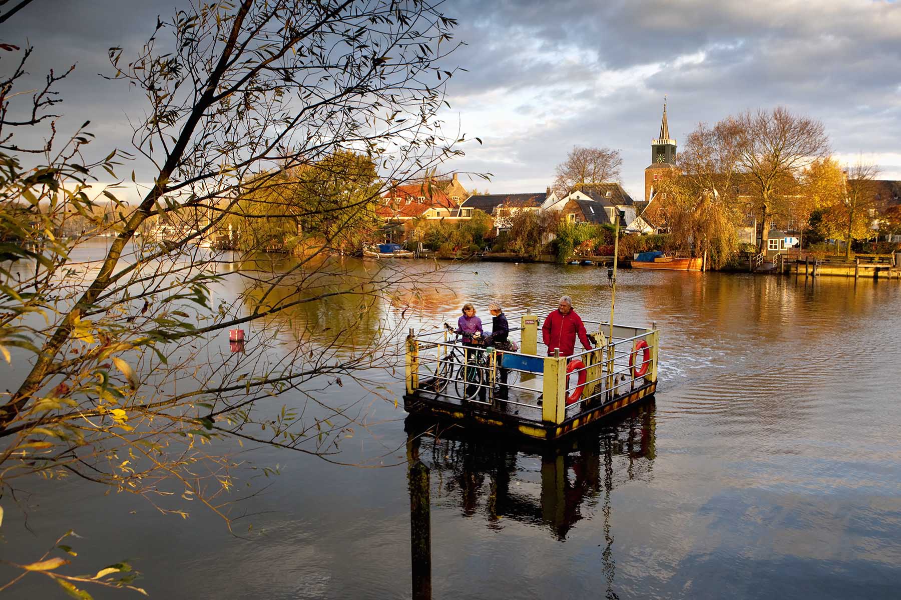 Group of people stnading on a small pond ferry to cross a river in the Netherlands.