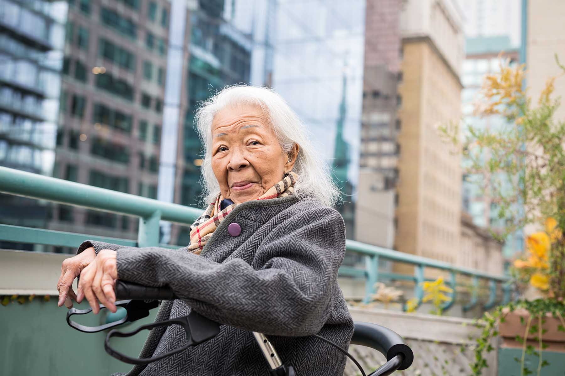 Old lady sitting in her mobility walker while looking at the camera. She's sitting on a rooftop patio on an autumn day.