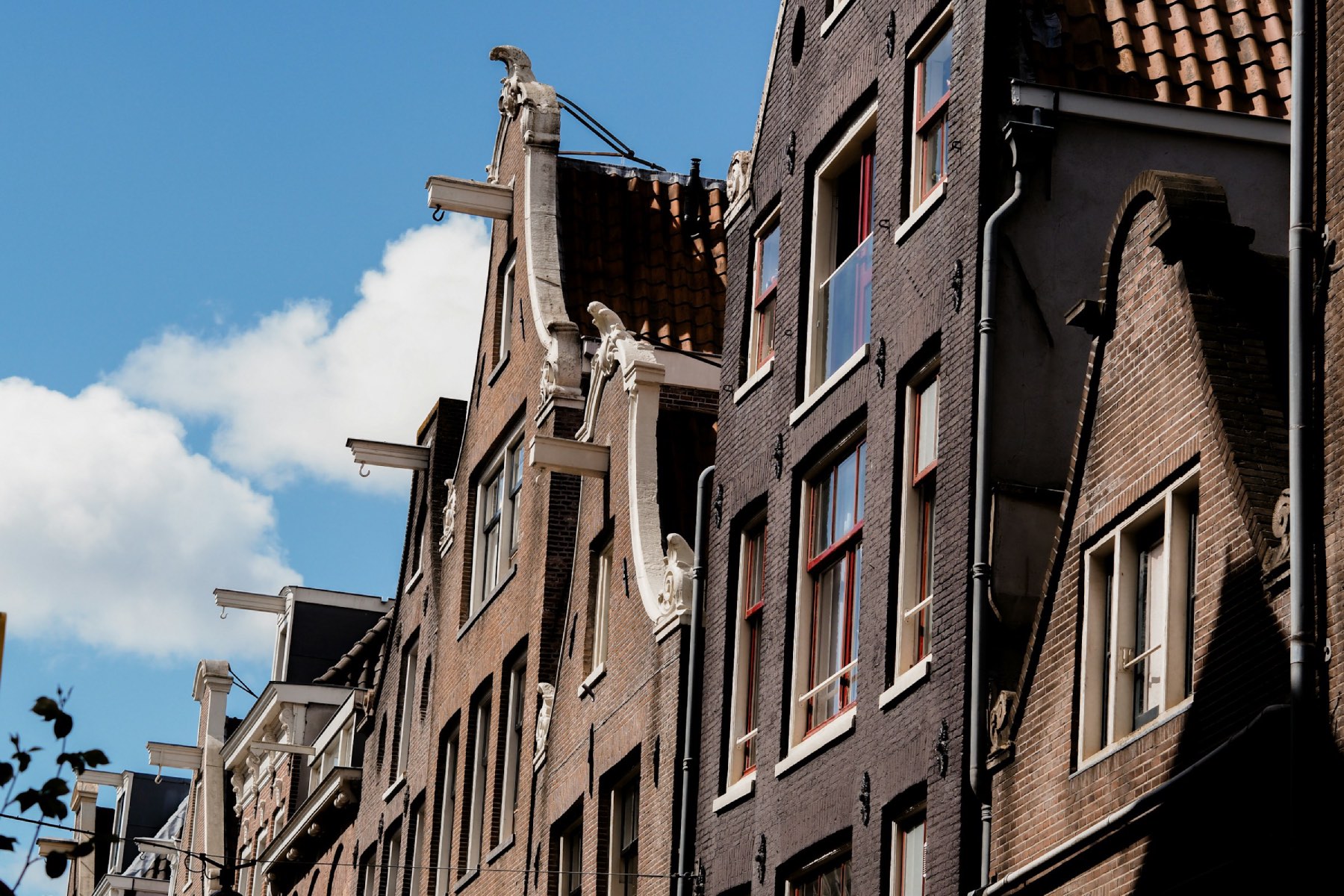 Gabled houses in Amsterdam with beams and iron hooks sticking out from the top against a bright blue sky
