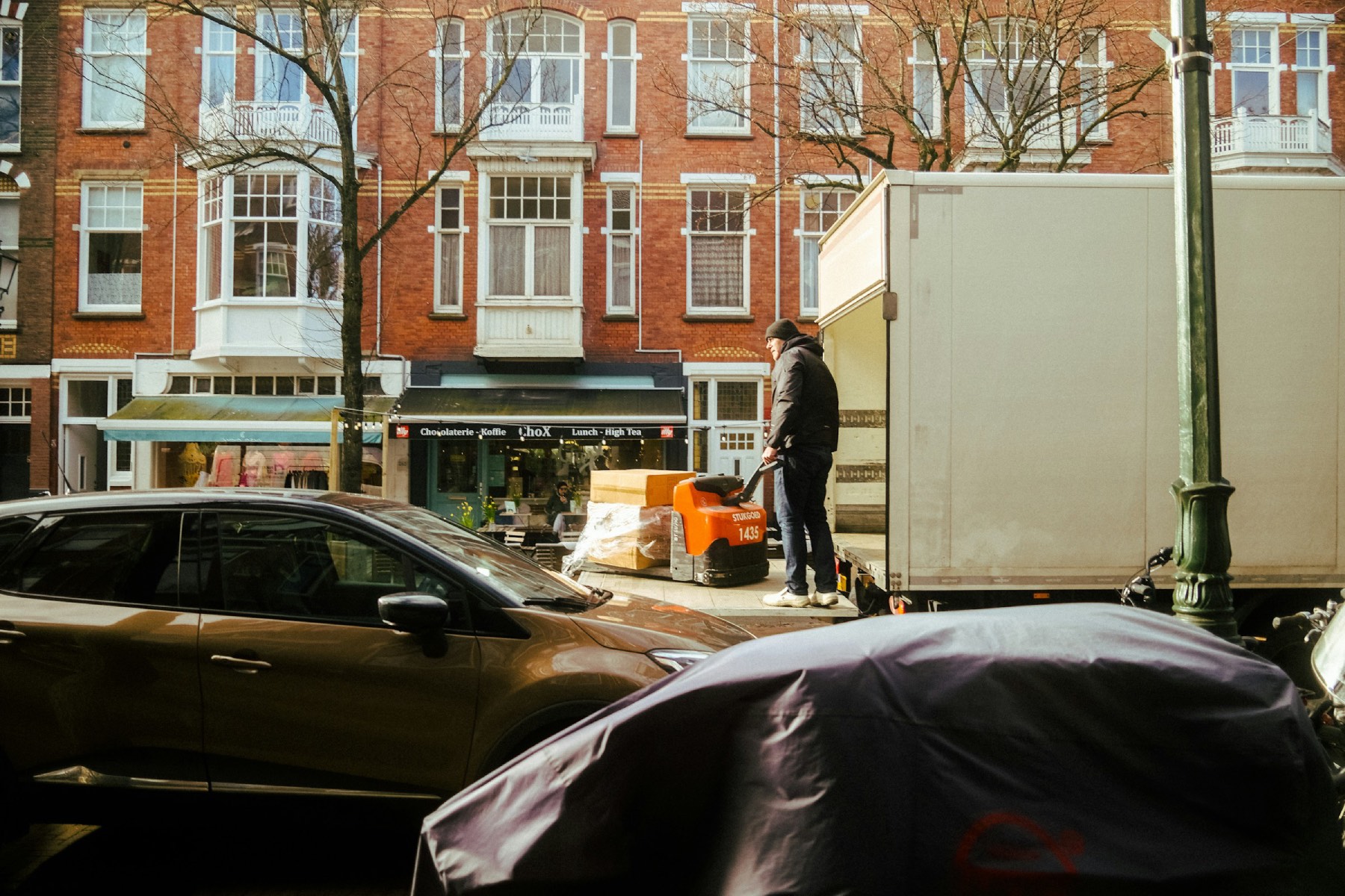 A man unloads boxes from a white moving van in Amsterdam next to moving traffic