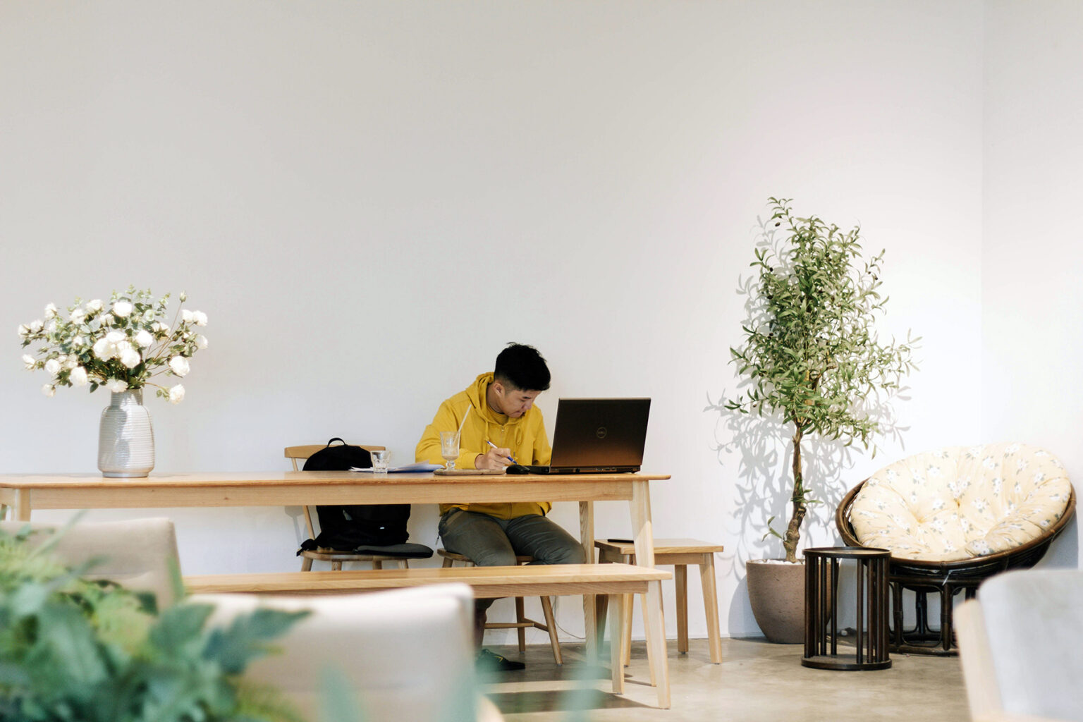 Man in a yellow hoodie sitting at a table in front of a laptop.