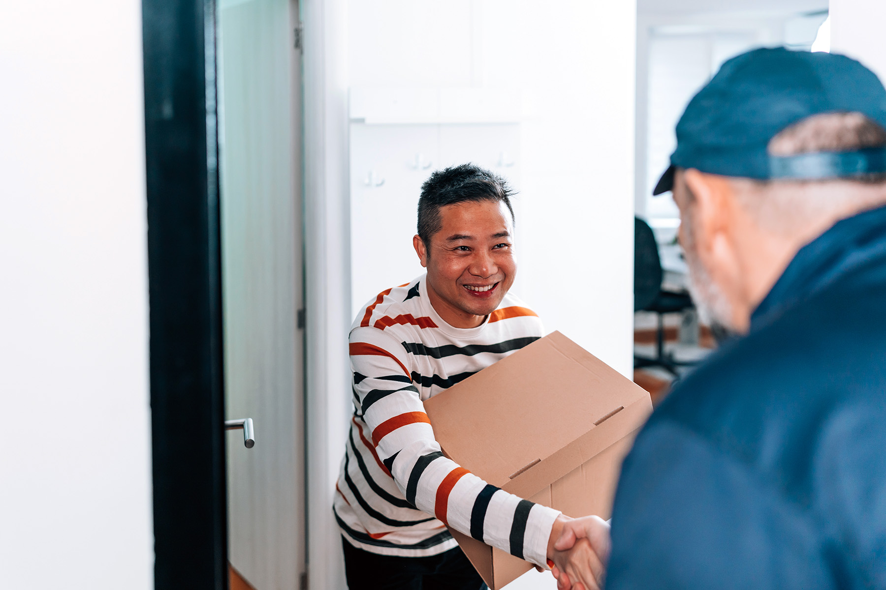 Happy man receiving a package in the mail and shaking hands with the delivery man.