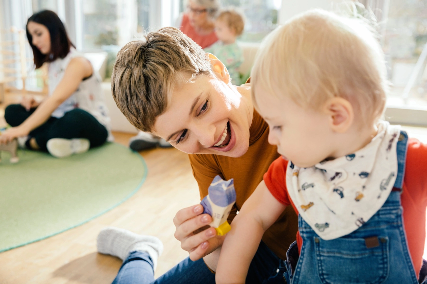 a carer looking after a small baby at a daycare center, smiling and holding a toy